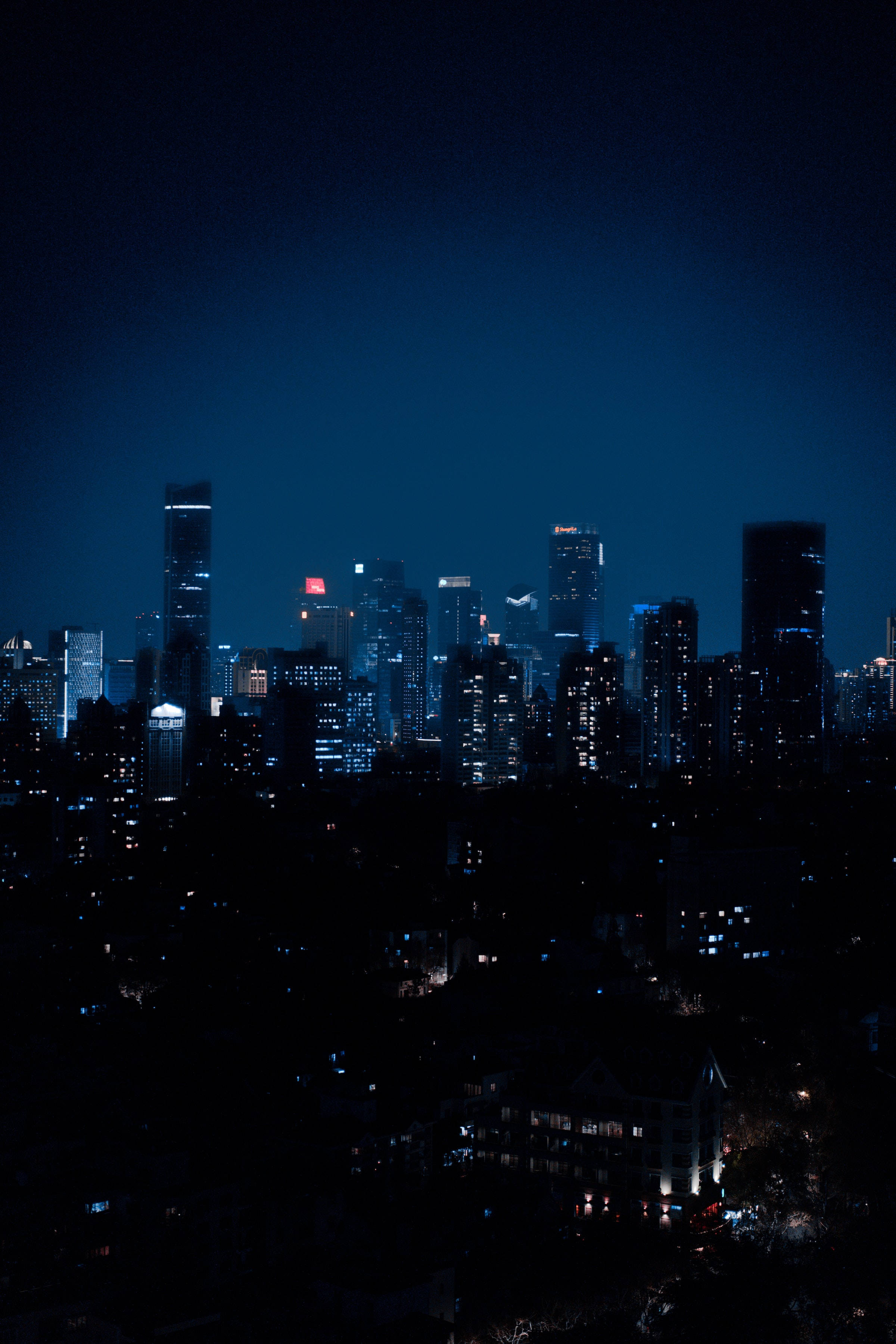 夜空 桌布 壁紙 — 高聳的城市天際線在深靛藍色的夜空下閃爍著電光藍和溫暖的黃色燈光。