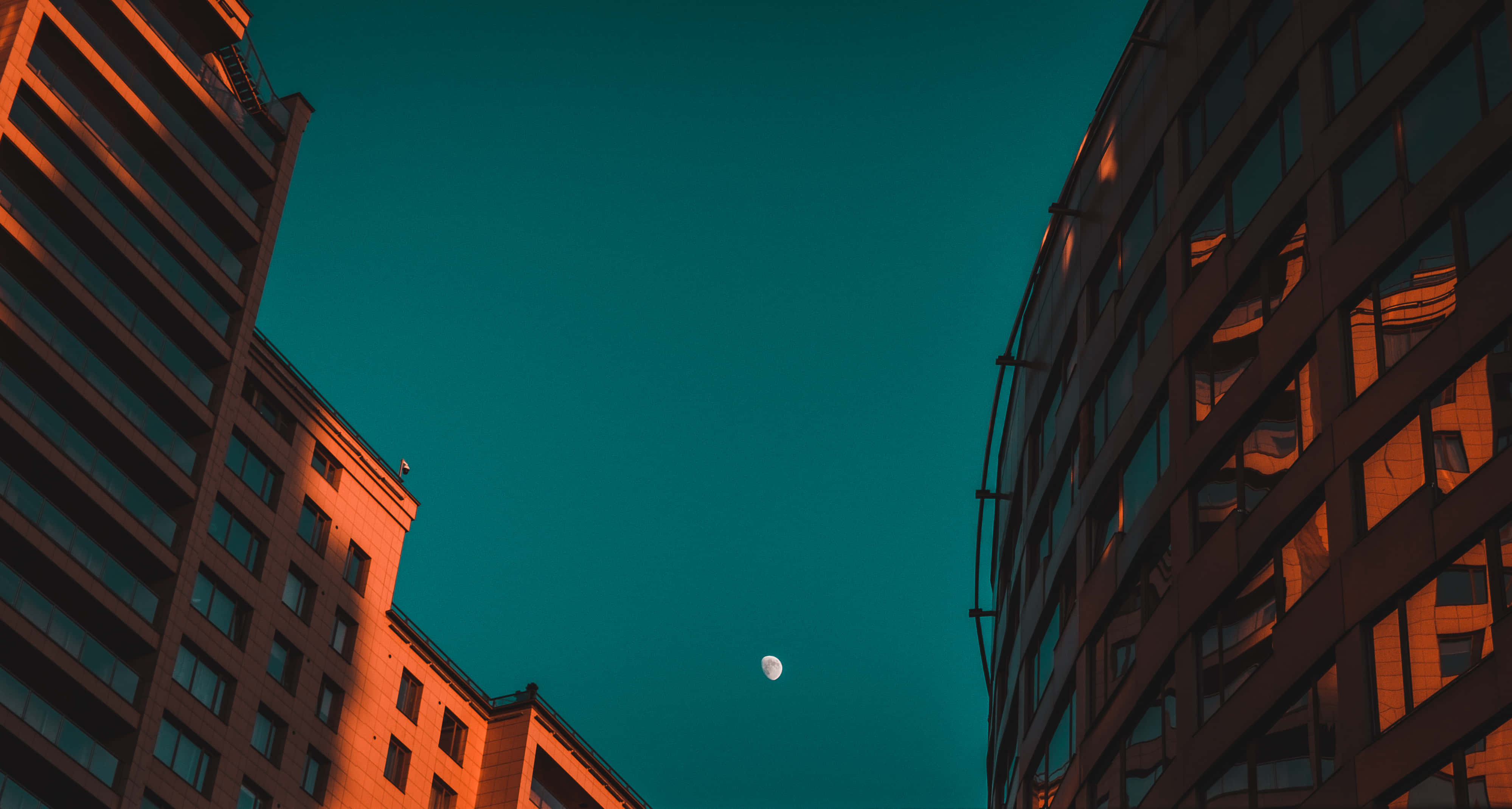 Buildings 桌布 壁紙 — 高聳的城市建築勾勒出一彎新月，映襯著深藍綠色的暮色天空。