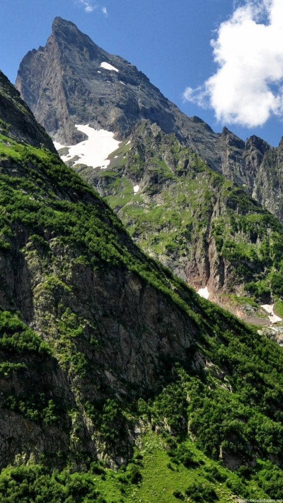 Nature iPhone 桌布 壁紙 — 高聳的岩石山峰，帶有雪斑，在明亮的藍天下有蓬鬆的白雲。