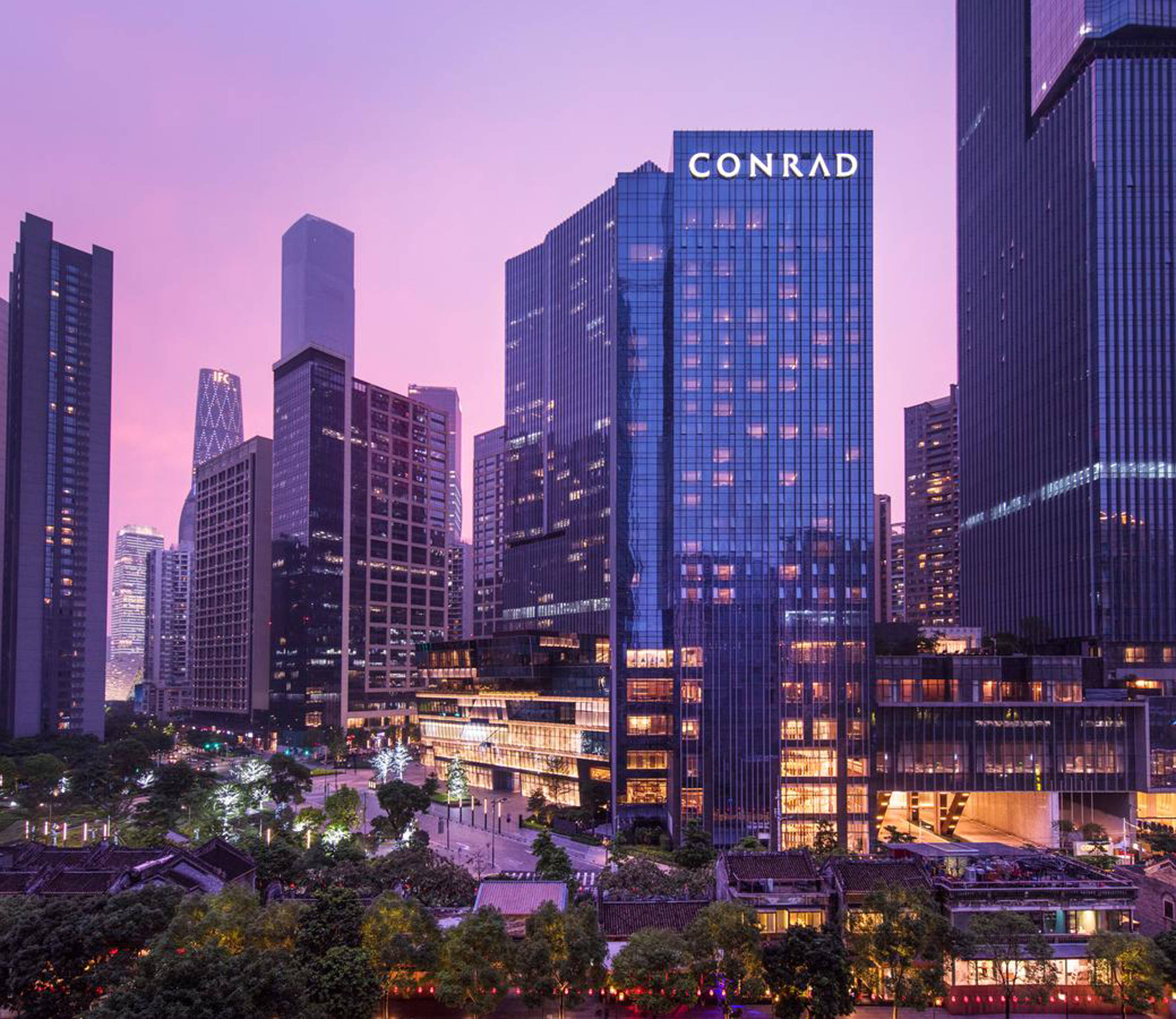 Guangzhou 桌布 壁紙 — 高聳的康萊德酒店在紫色暮色天空下閃耀著溫暖的燈光，融入密集的現代城市景觀。