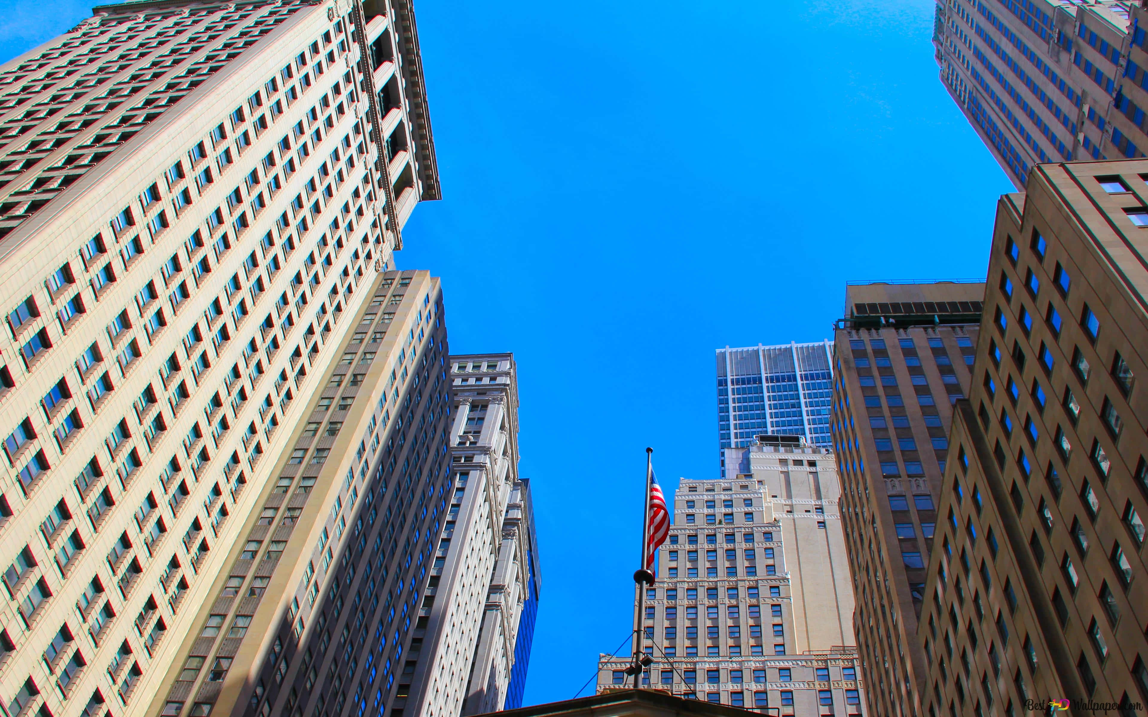 Wall Street 桌布 壁紙 — 高聳的摩天大樓刺穿充滿活力的藍天，低角度城市拍攝，可見美國國旗。
