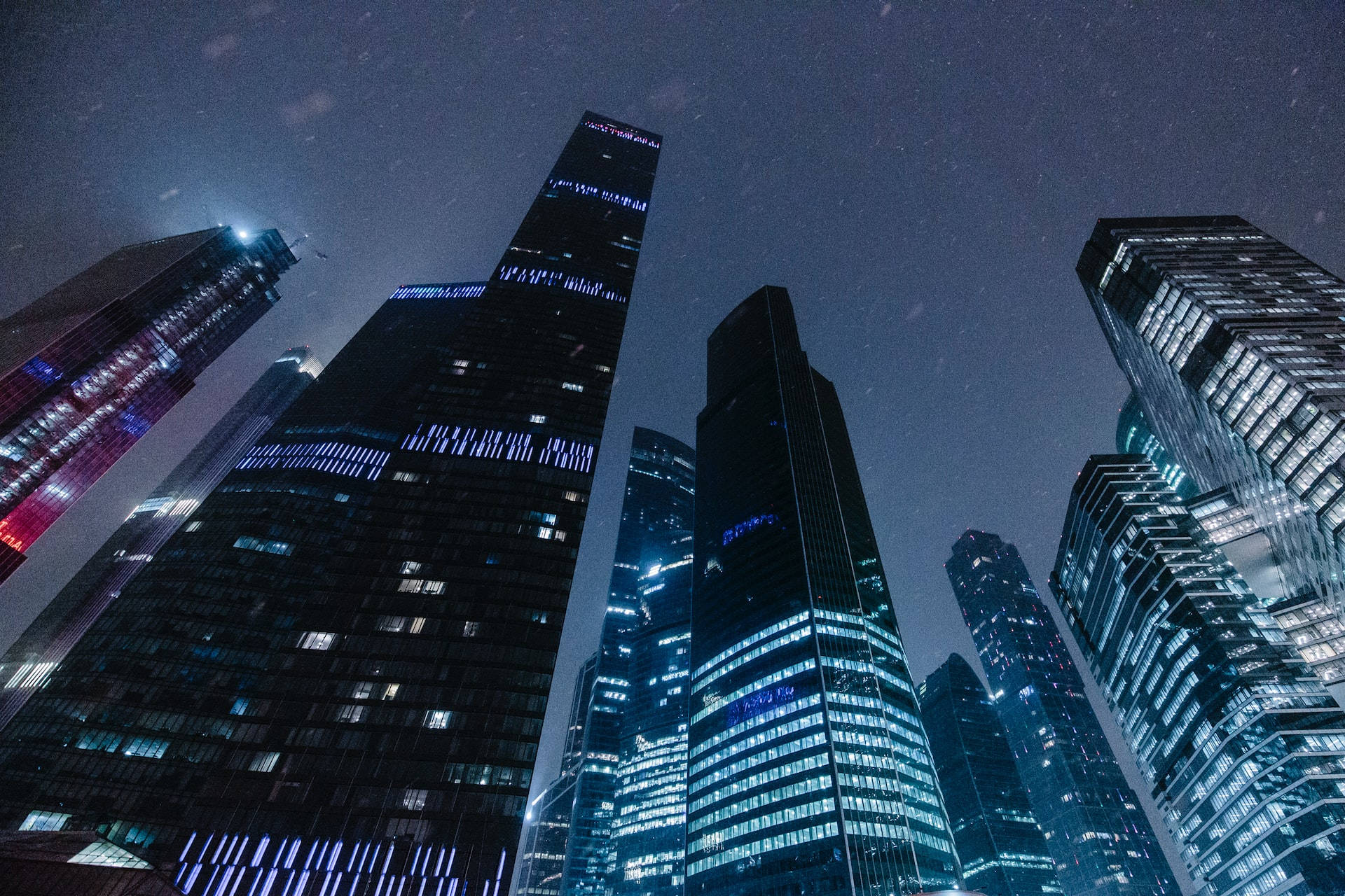Skyscraper 桌布 壁紙 — 高聳的摩天大樓刺穿繁星點點的夜空，發光的窗戶和霓虹燈在玻璃外牆上反射。