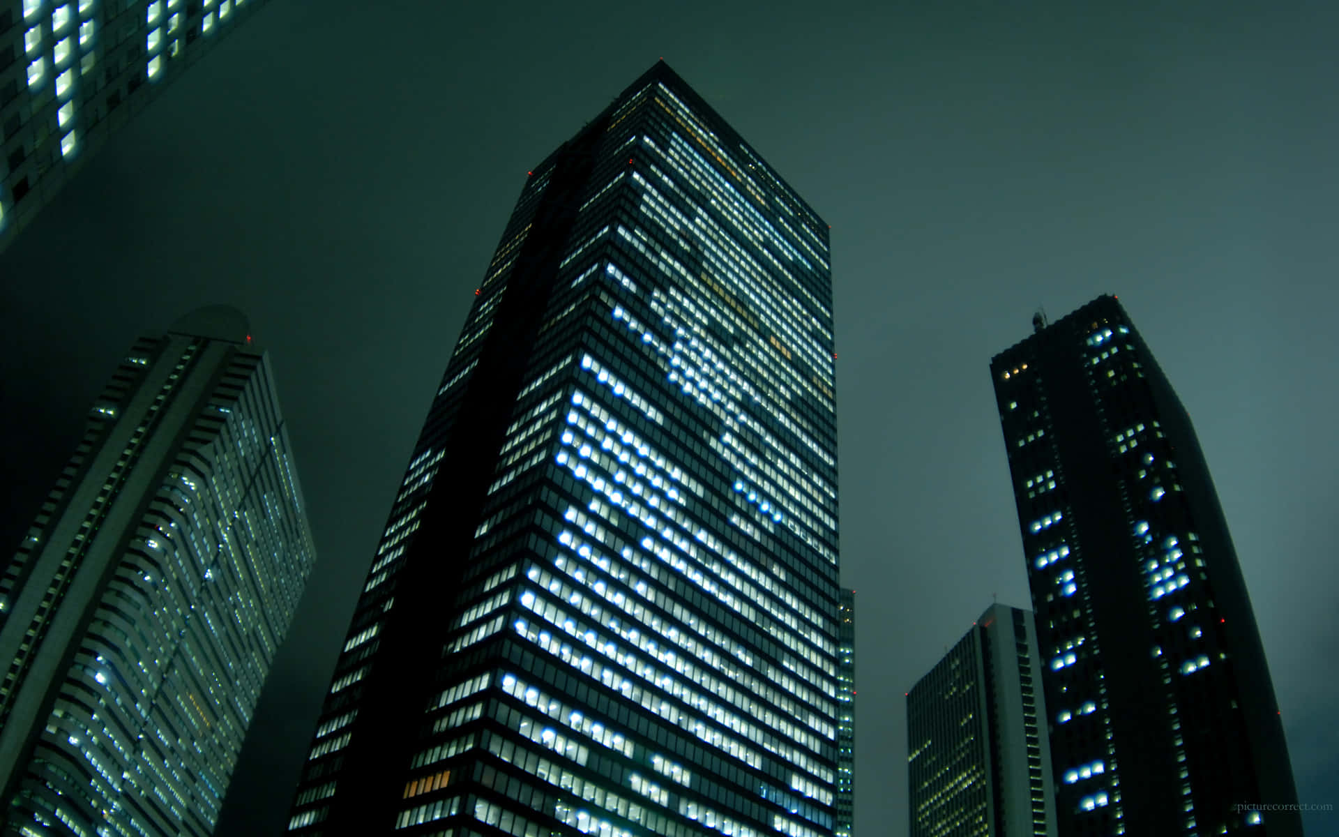 Modern Desktop 桌布 壁紙 — 高聳的摩天大樓刺穿黑暗的夜空，它們的窗戶在陰沉的灰色薄霧中閃爍著藍色和白色的燈光。