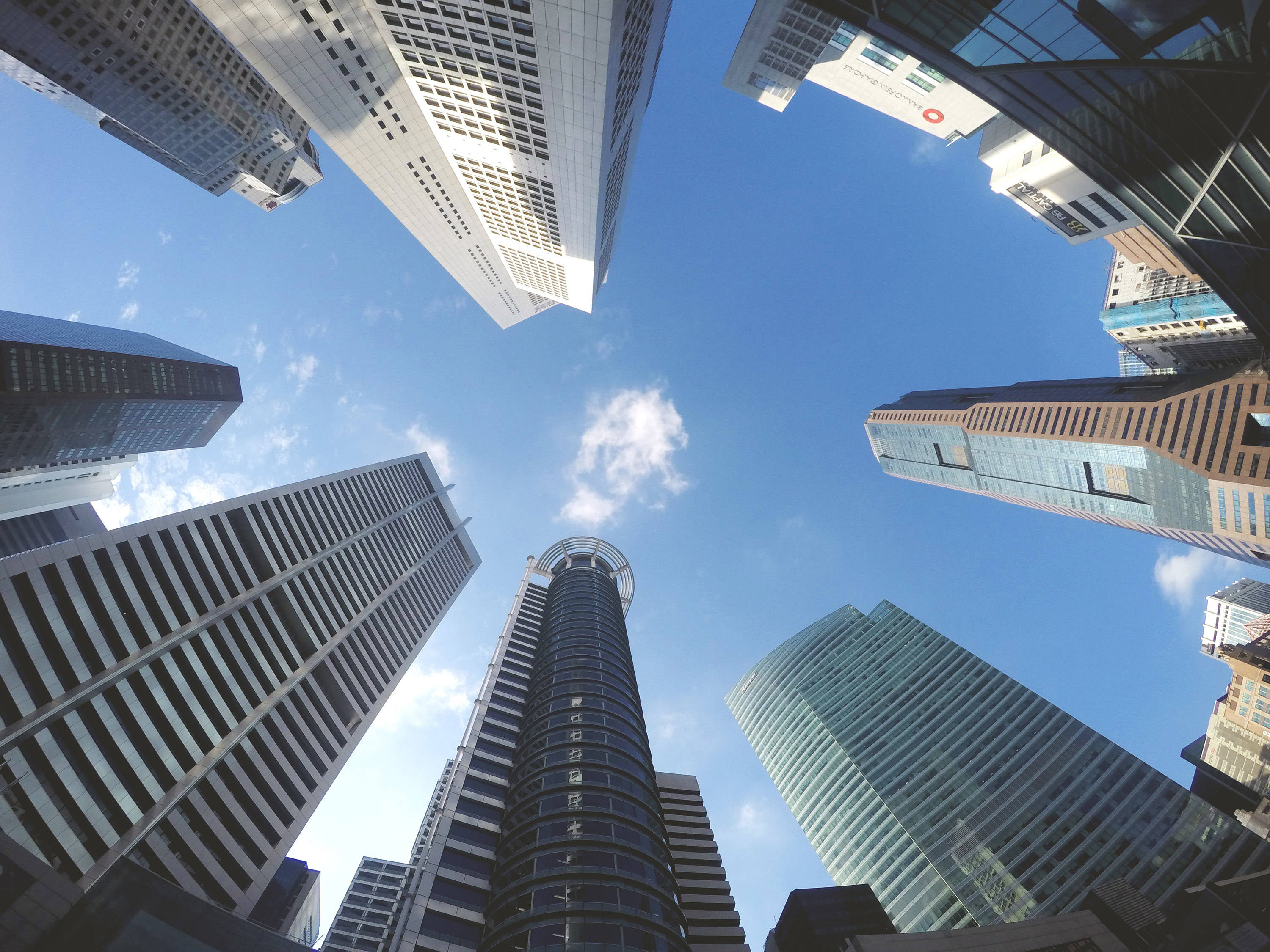 Buildings 桌布 壁紙 — 高聳的摩天大樓匯聚向明亮的藍天，天空中有散落的雲朵，呈現戲劇性的低角度城市拍攝。