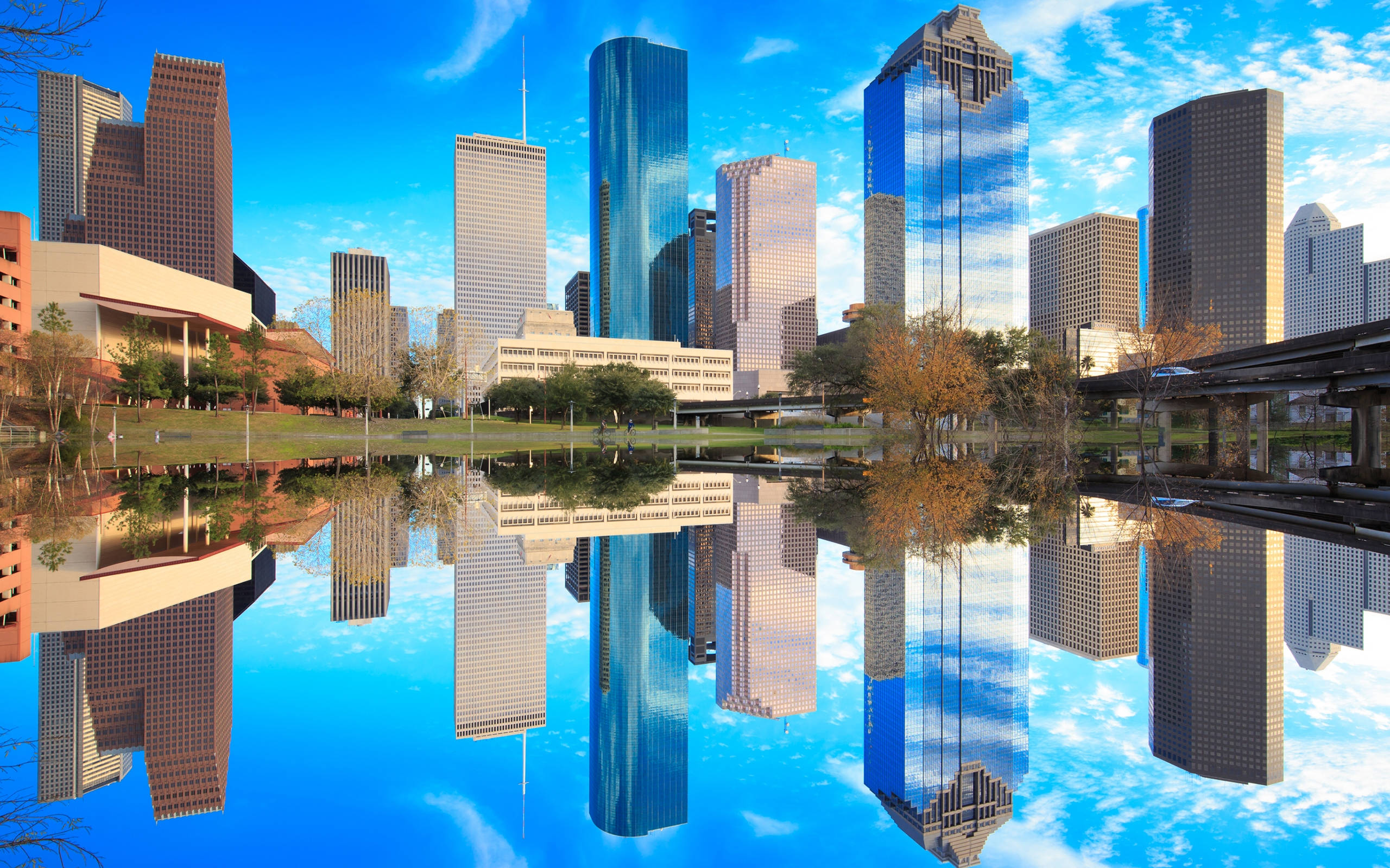 Houston 桌布 壁紙 — 高聳的摩天大樓在晴朗藍天和零星白雲下，完美倒映在平靜的池塘中。