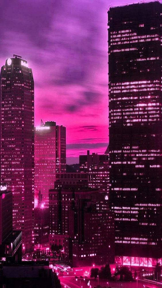 Pink Neon Aesthetic 桌布 壁紙 — 高聳的摩天大樓在暮色中散發著電光粉紅的光芒，映襯著超現實的洋紅色天空。