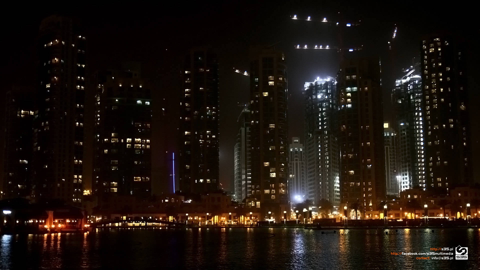 Qatar 桌布 壁紙 — 高聳的摩天大樓在漆黑的夜空中散發著溫暖的光芒，它們的倒影在平靜的水面上閃爍。