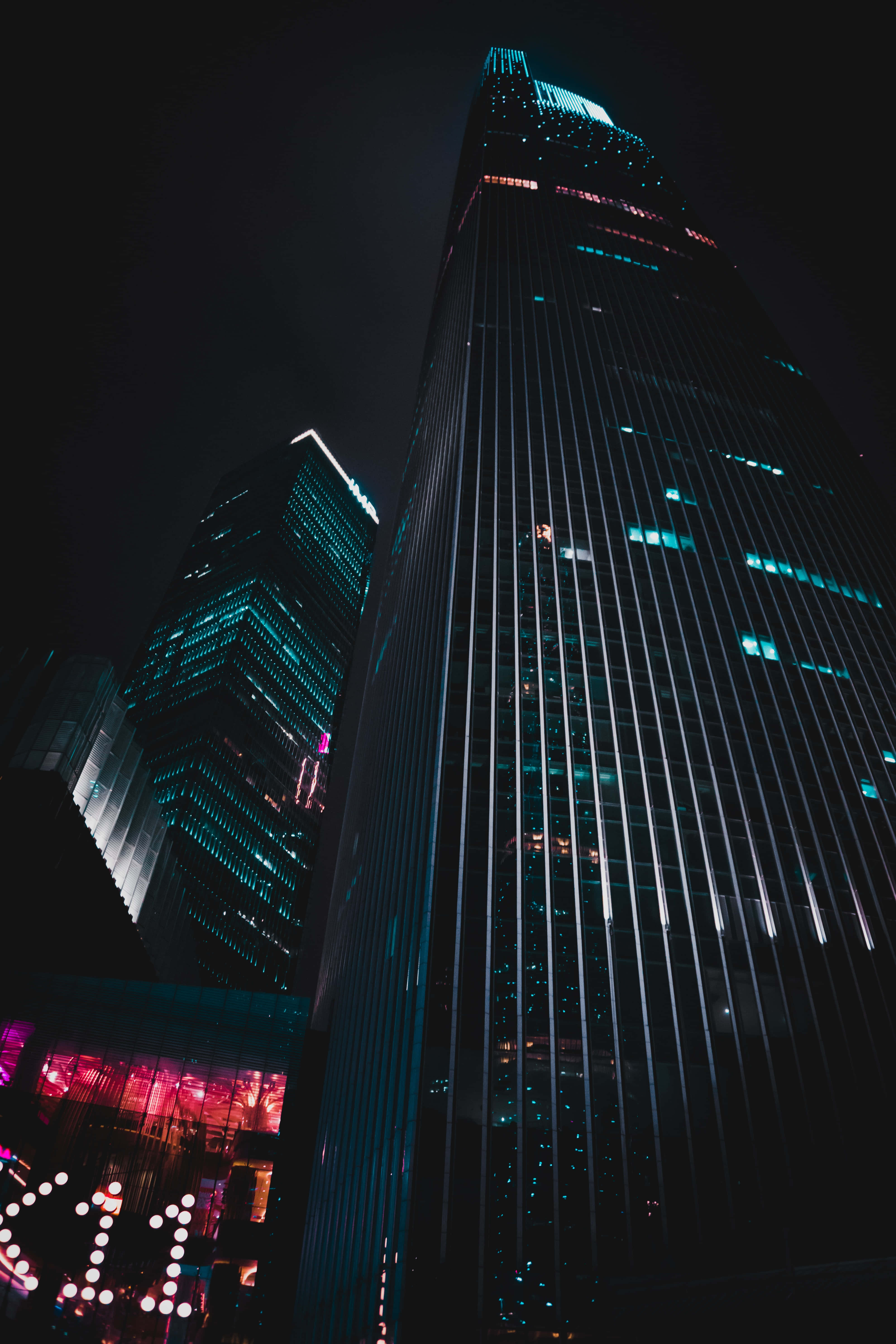Building 桌布 壁紙 — 高聳的摩天大樓在黑暗的城市畫布上，以發光的藍色和粉紅色霓虹燈刺穿夜空。