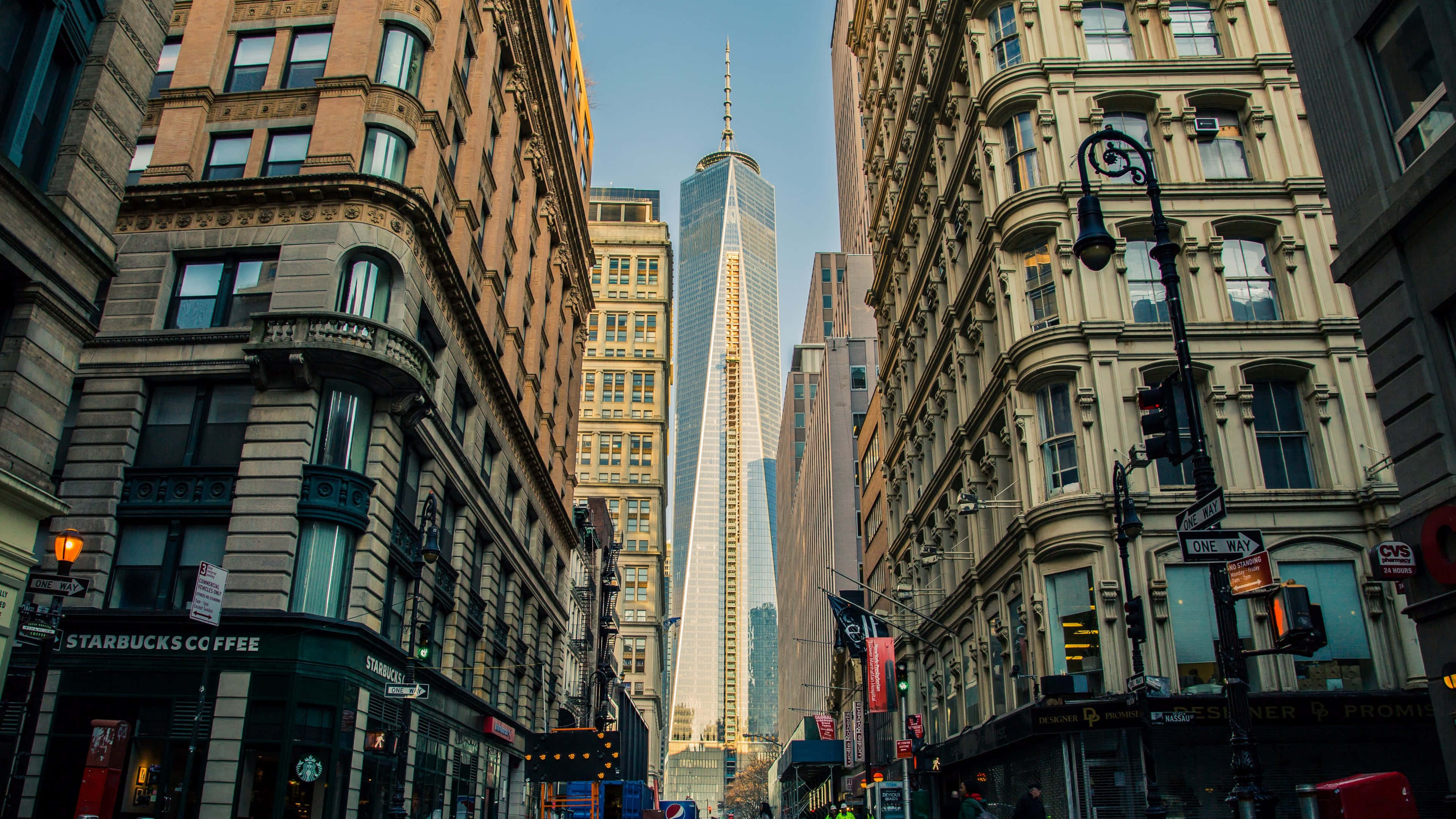 Skyscraper 桌布 壁紙 — 高聳的摩天大樓框住一條狹窄的城市街道，在晴朗的藍天下通往標誌性的世界貿易中心一號樓。