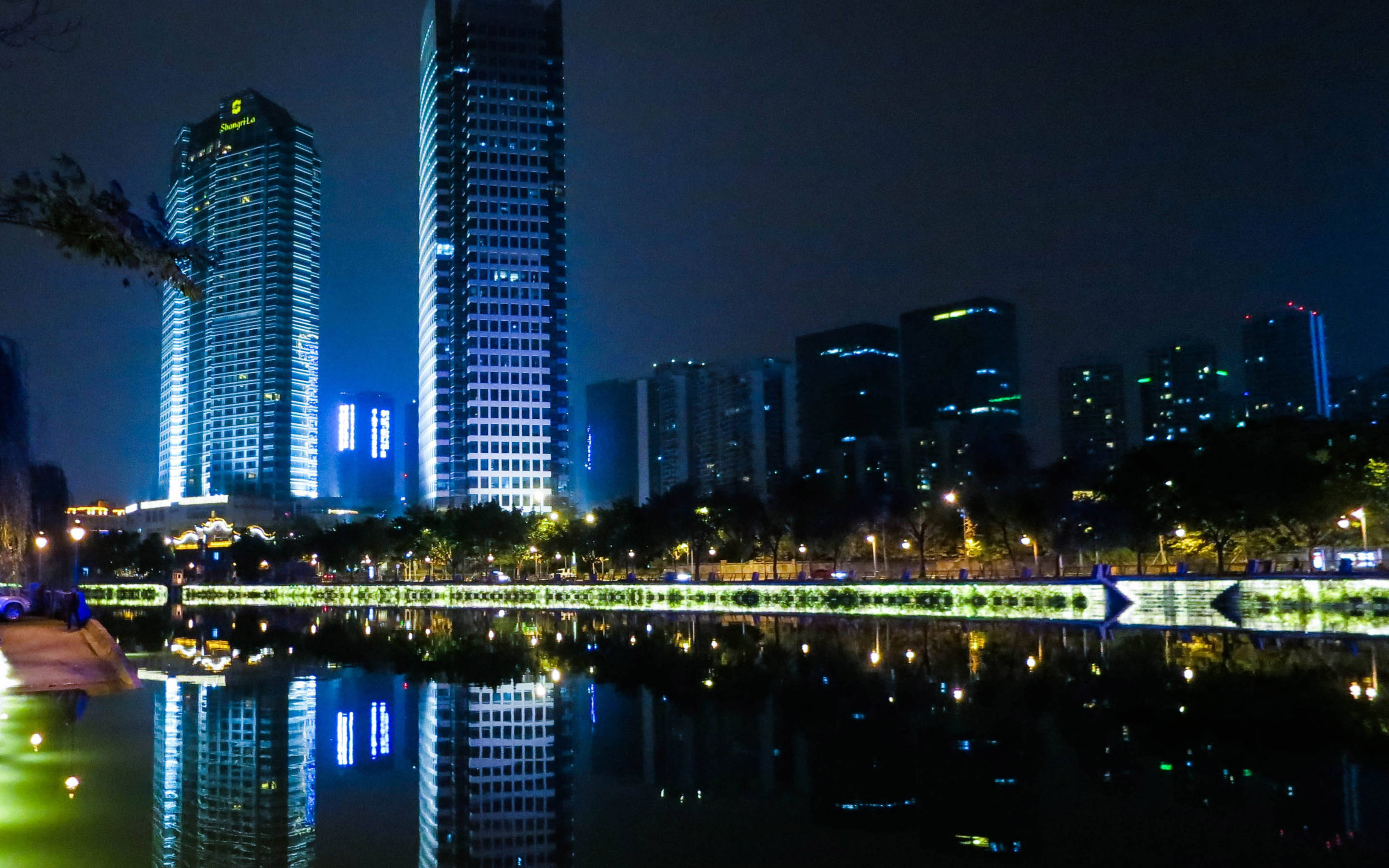 Chengdu 桌布 壁紙 — 高聳的摩天大樓發出藍色和白色的燈光，倒映在夜晚寧靜的城市湖中。