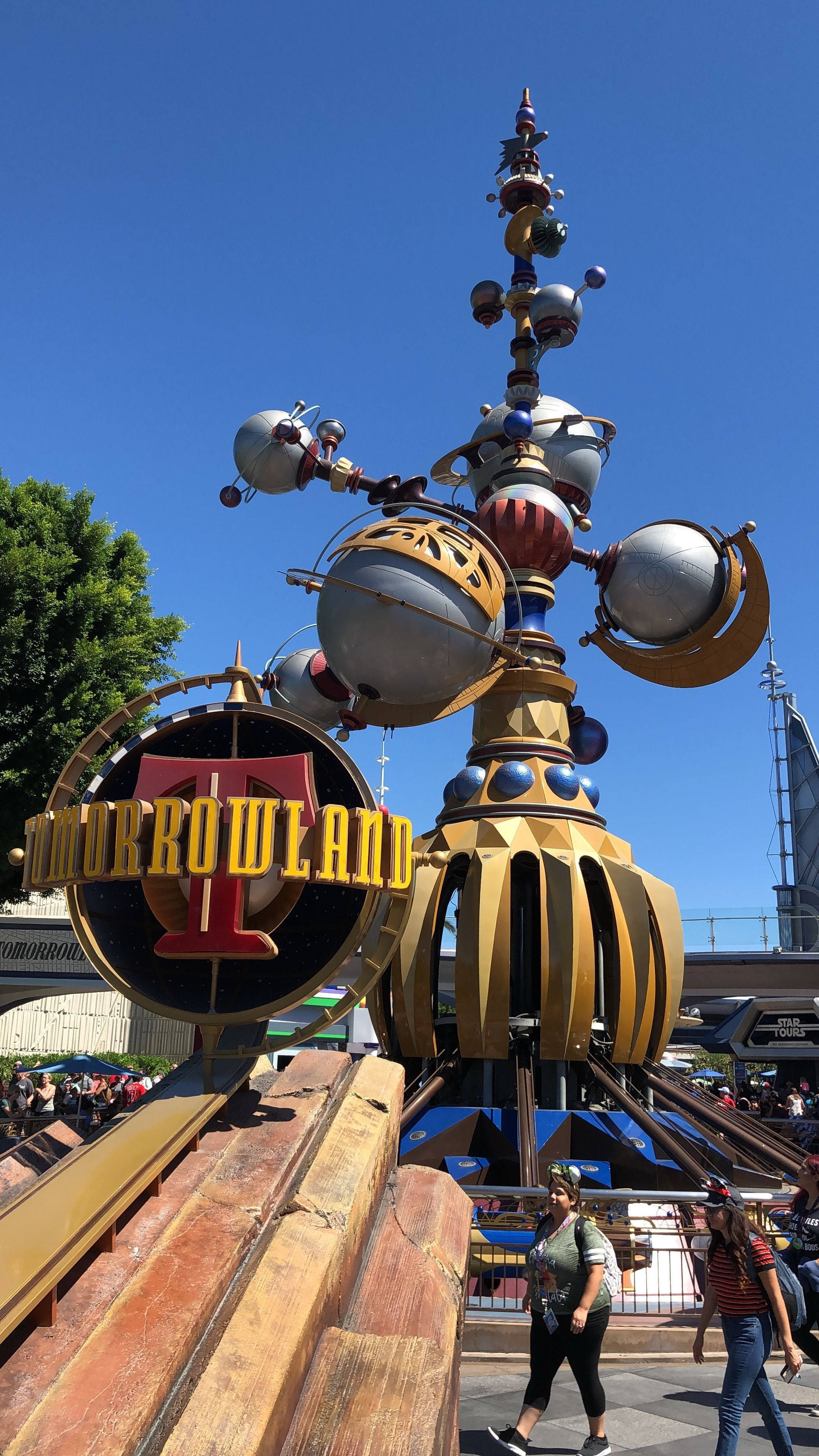 Tomorrowland Movie 桌布 壁紙 — 高聳的明日世界入口標誌，帶有金屬球體和一個醒目的紅色T，背景是清澈的藍天。
