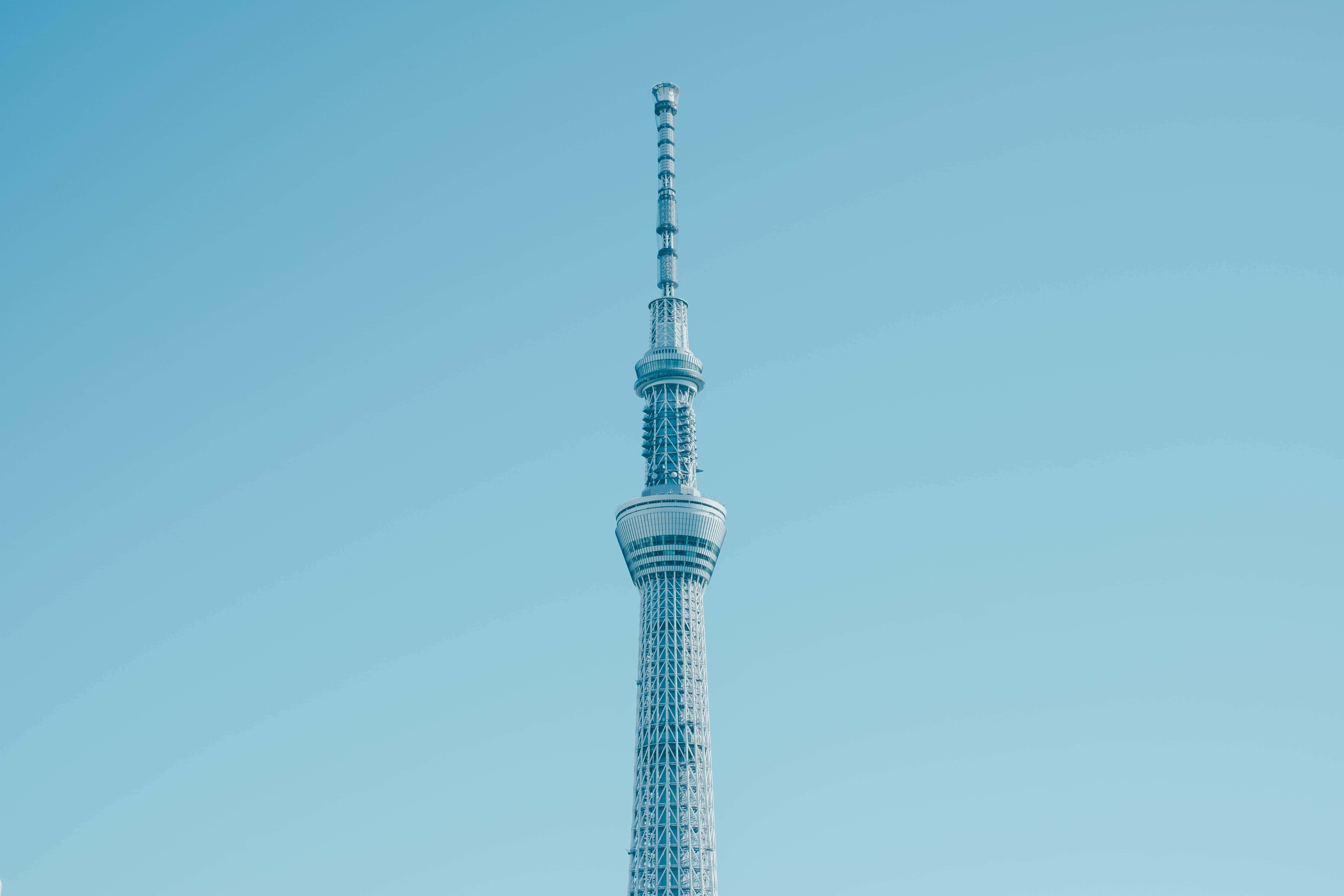 Solid Light Blue 桌布 壁紙 — 高聳的東京晴空塔以其複雜的格子結構和天線陣列刺穿清澈的漸變藍天。
