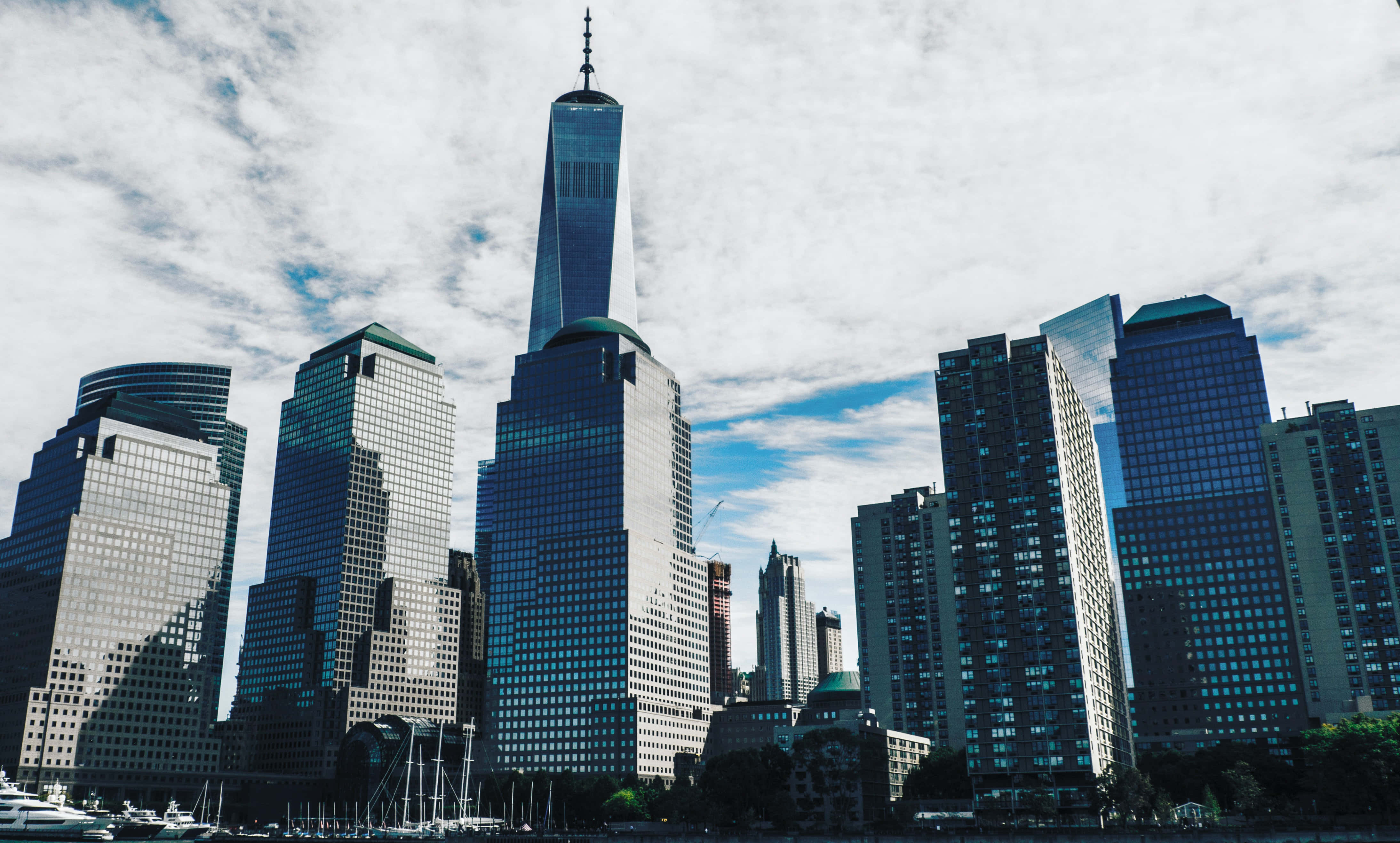 Skyscraper 桌布 壁紙 — 高聳的玻璃摩天大樓刺穿部分多雲的天空，世界貿易中心一號大樓主導著現代城市天際線。