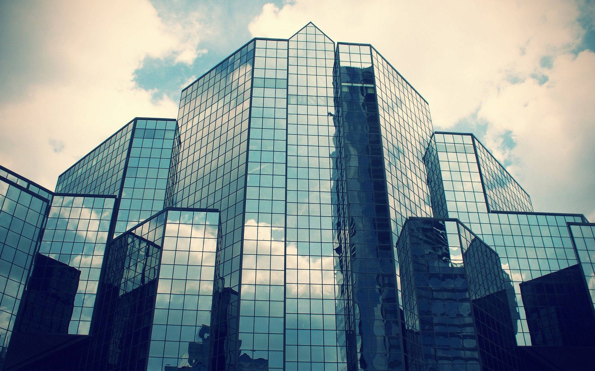 Building 桌布 壁紙 — 高聳的玻璃摩天大樓反射多雲的天空，營造出戲劇性的低角度城市景觀。