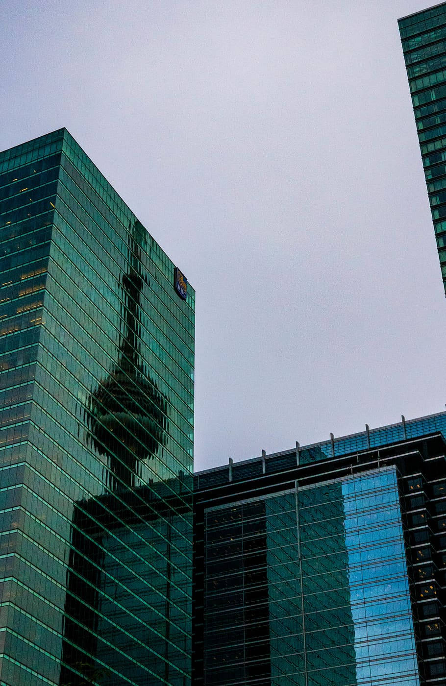 Skyscraper 桌布 壁紙 — 高聳的玻璃摩天大樓在其青綠色的窗戶中反射出多雲的天空和遠處的塔樓。