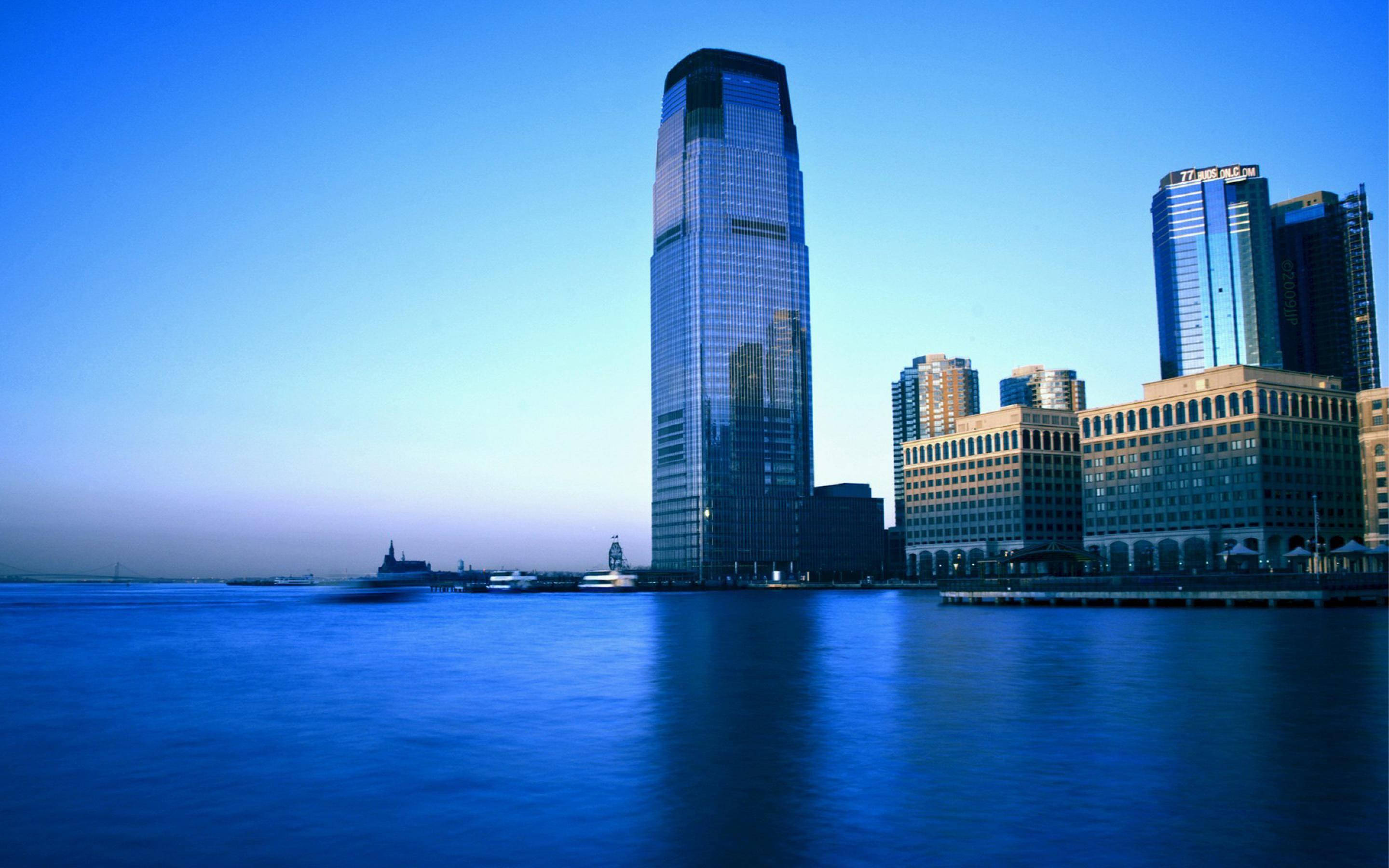 Skyscraper 桌布 壁紙 — 高聳的玻璃摩天大樓在暮色中倒映在平靜的水面上，映照出清澈的藍天。