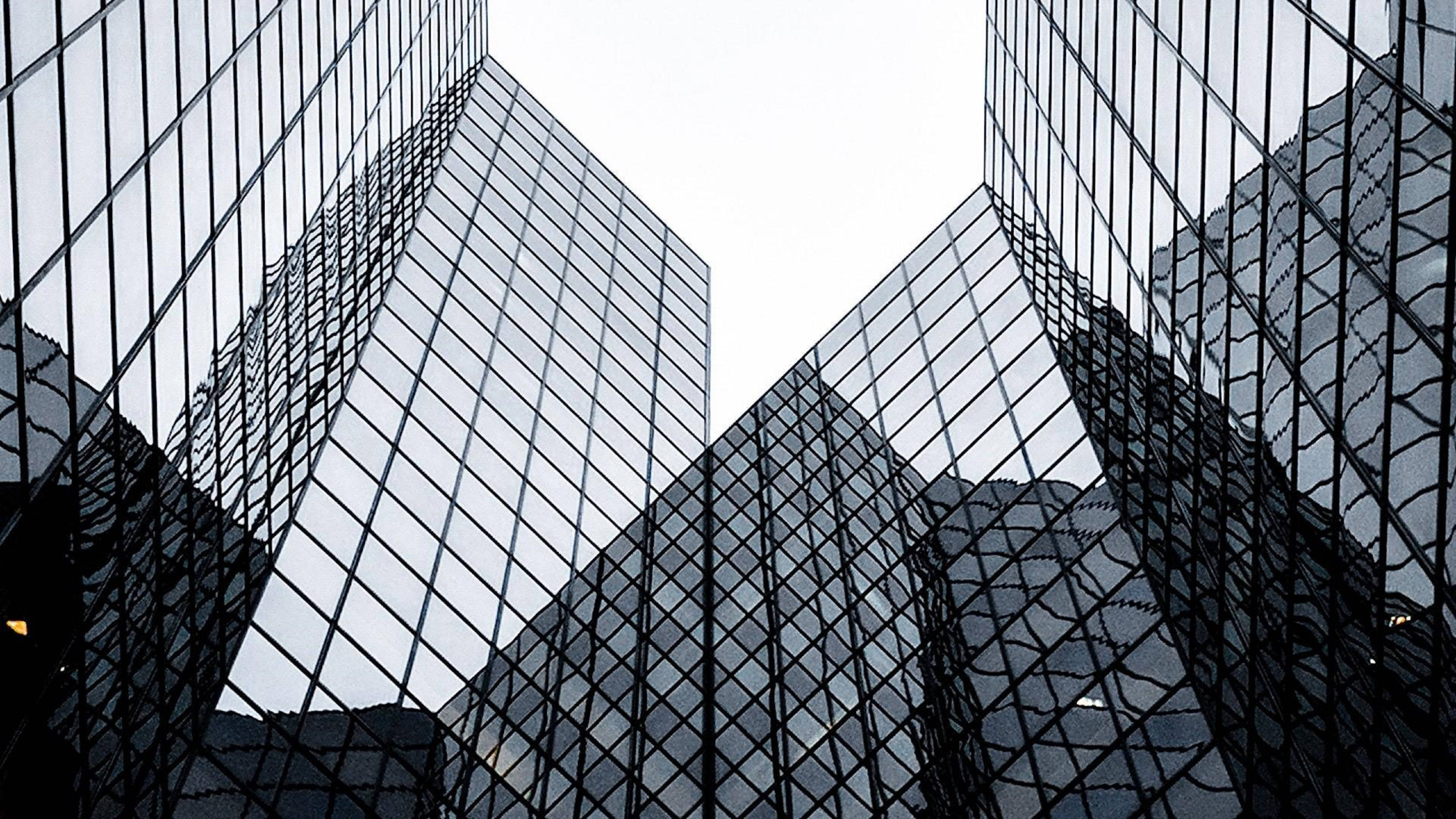 Architecture 桌布 壁紙 — 高聳的玻璃摩天大樓在蒼白的天空下以嚴格的幾何圖案向上匯聚。