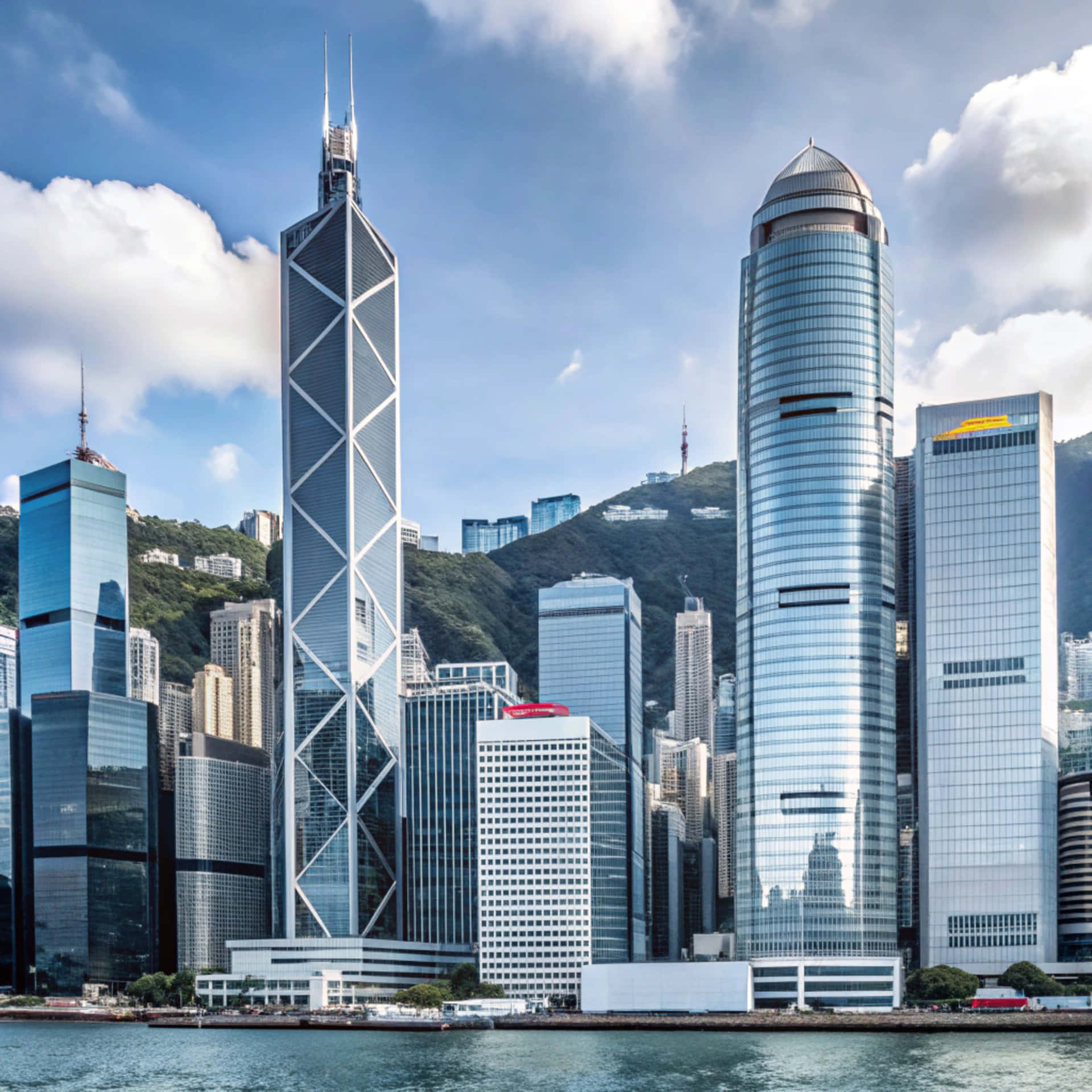 Hong Kong skyline 壁紙 — 高聳的玻璃摩天大樓映照著藍天白雲，背景是翠綠的山丘和寧靜的水面。