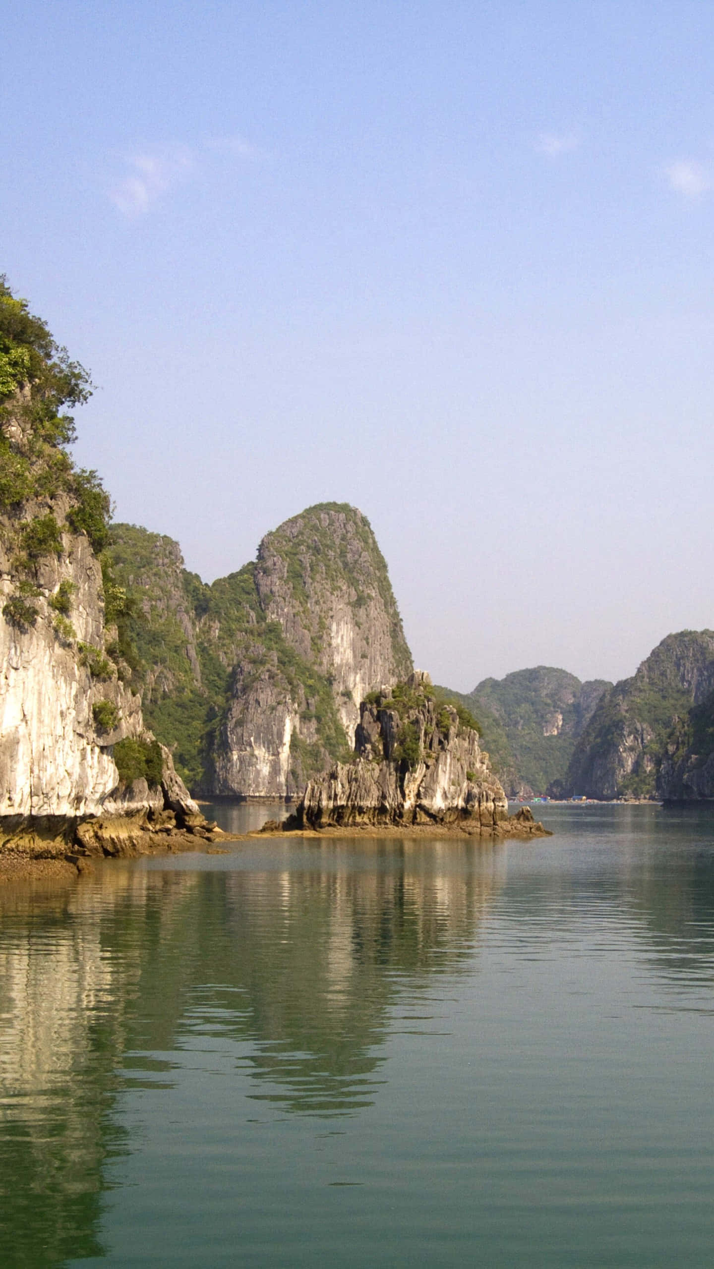 Vietnam 桌布 壁紙 — 高聳的石灰岩喀斯特地貌從平靜的碧綠海水中升起，在晴朗的藍天下，展現出寧靜的越南海灣景色。
