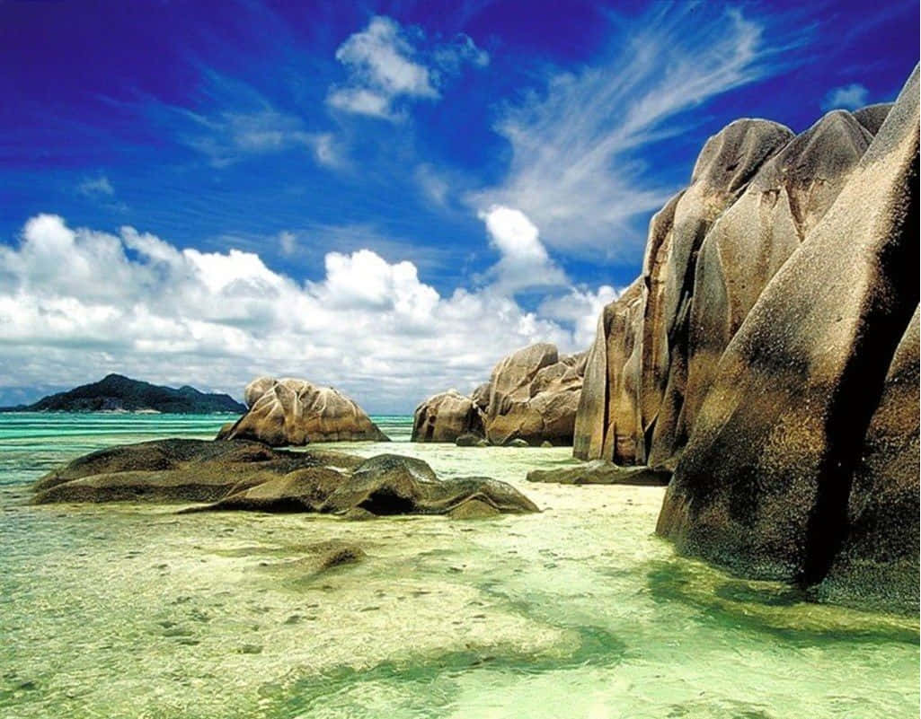Seychelles Beach 桌布 壁紙 — 高聳的花崗岩巨石從清澈的碧綠海水中升起，上方是藍天白雲。