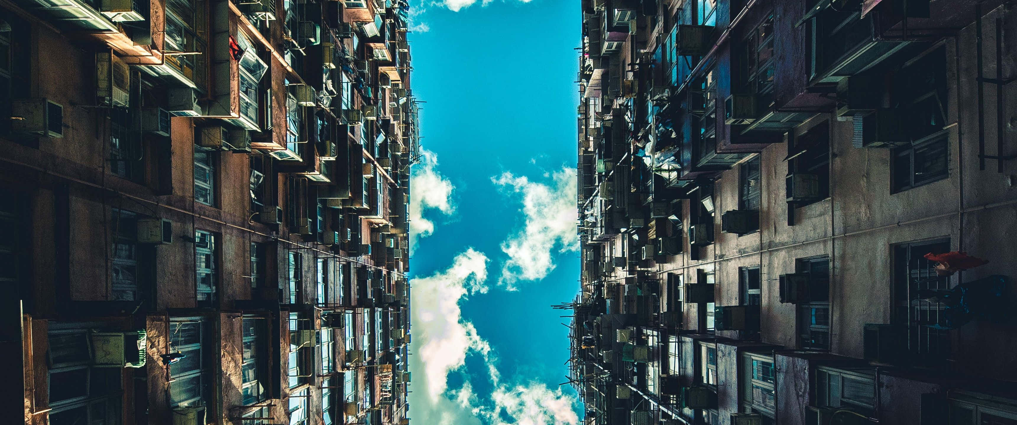 3440x1440p Seattle 桌布 壁紙 — 高聳的都市公寓大樓以戲劇性的低角度構圖，框住一片充滿活力的藍天和蓬鬆的白雲。