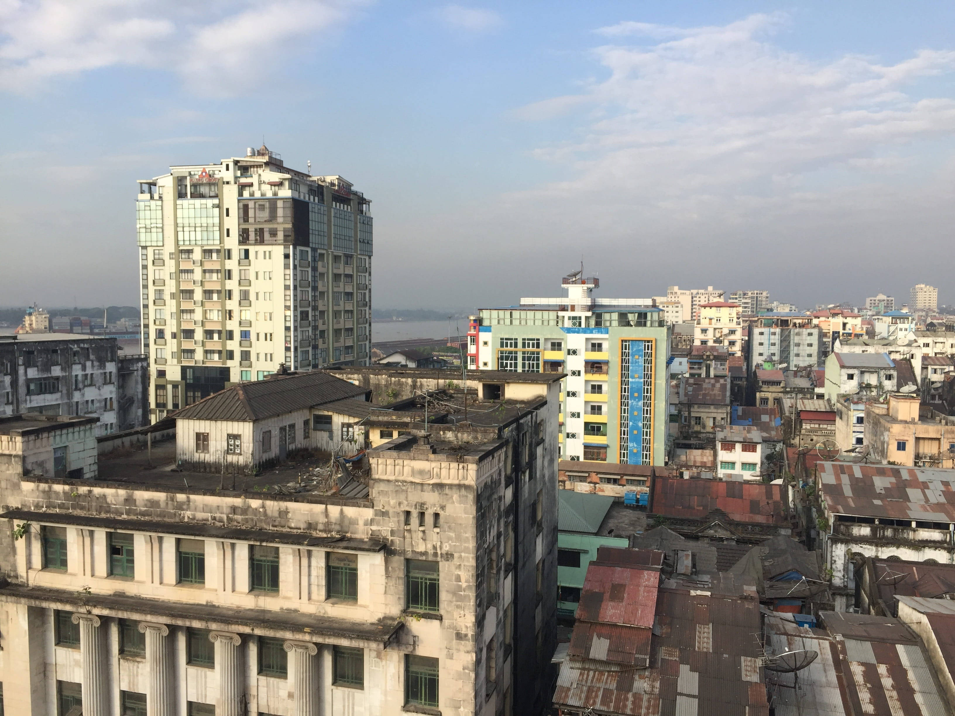 Yangon 桌布 壁紙 — 高角度俯瞰密集的城市天際線，建築物風化，混合現代與舊式建築，天空部分多雲。