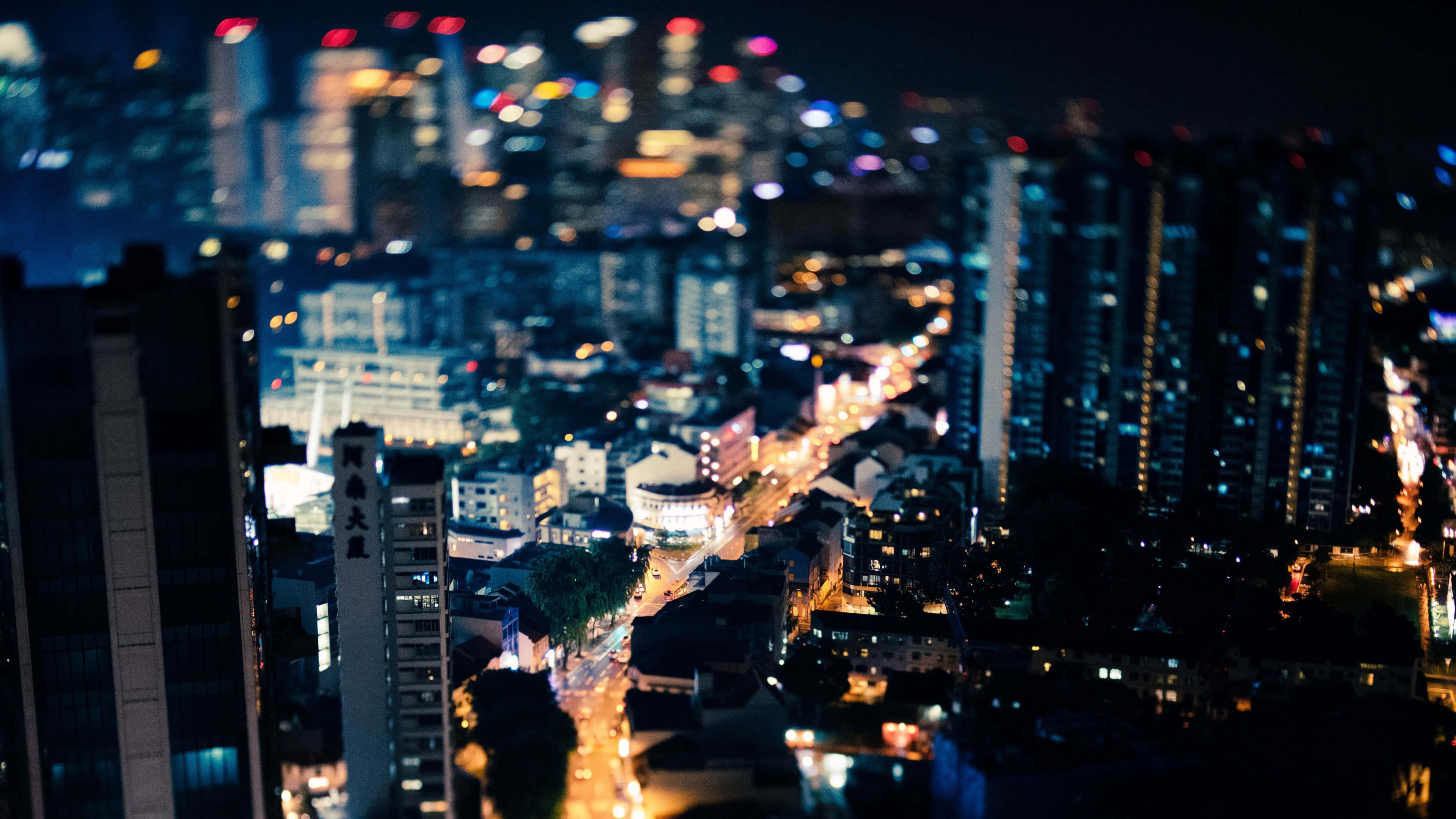 Lit iPhone 桌布 壁紙 — 高角度夜景城市景觀，發光的街燈和模糊的摩天大樓營造出微縮效果。