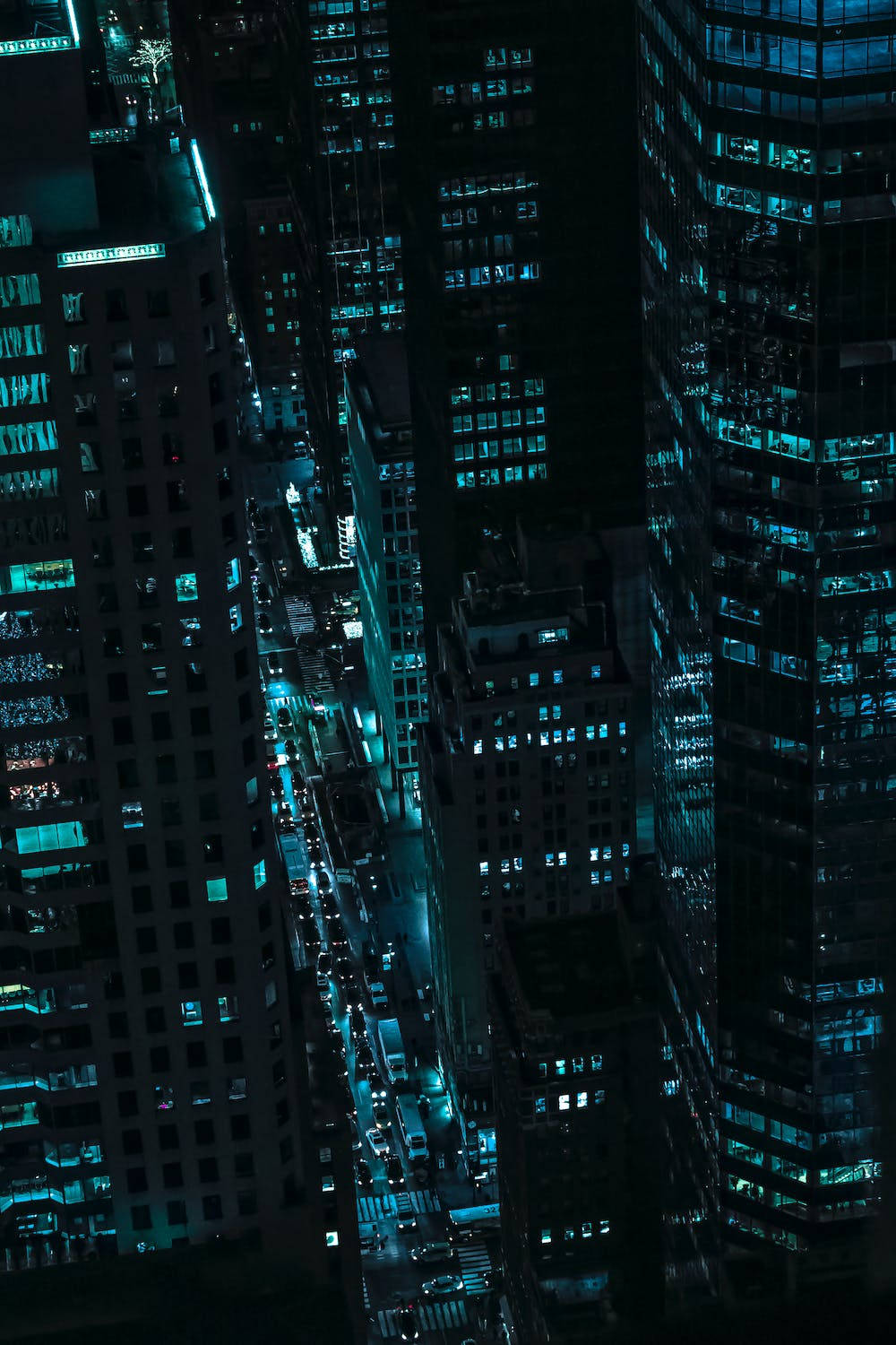 夜景城市 桌布 壁紙 — 高角度夜間景觀，密集的城市峽谷中，高聳的摩天大樓散發著冷藍色的光芒，照亮下方繁忙的街道。