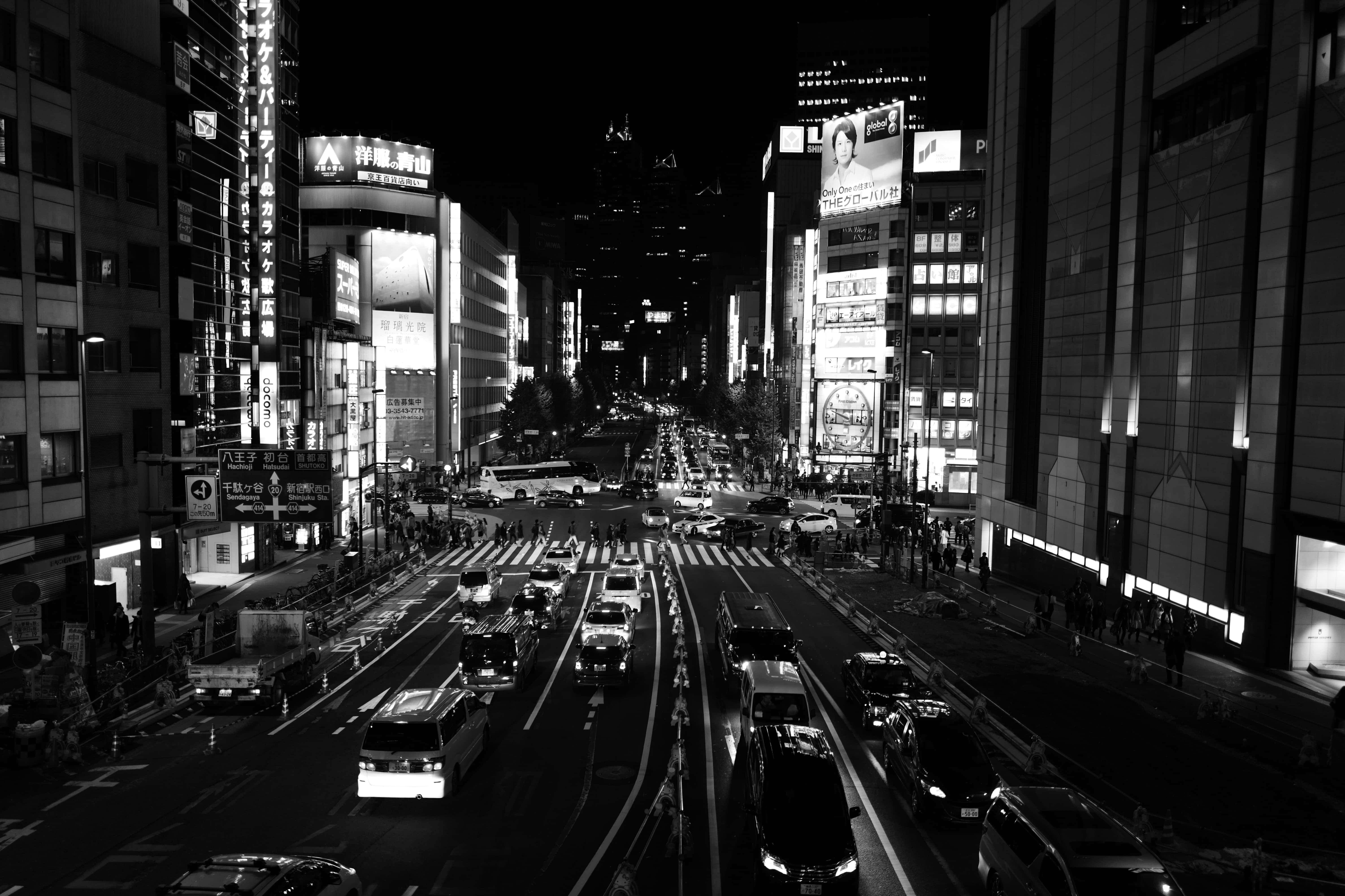 View 桌布 壁紙 — 高角度黑白拍攝，繁華霓虹燈照亮的城市街道夜景，有交通和行人。