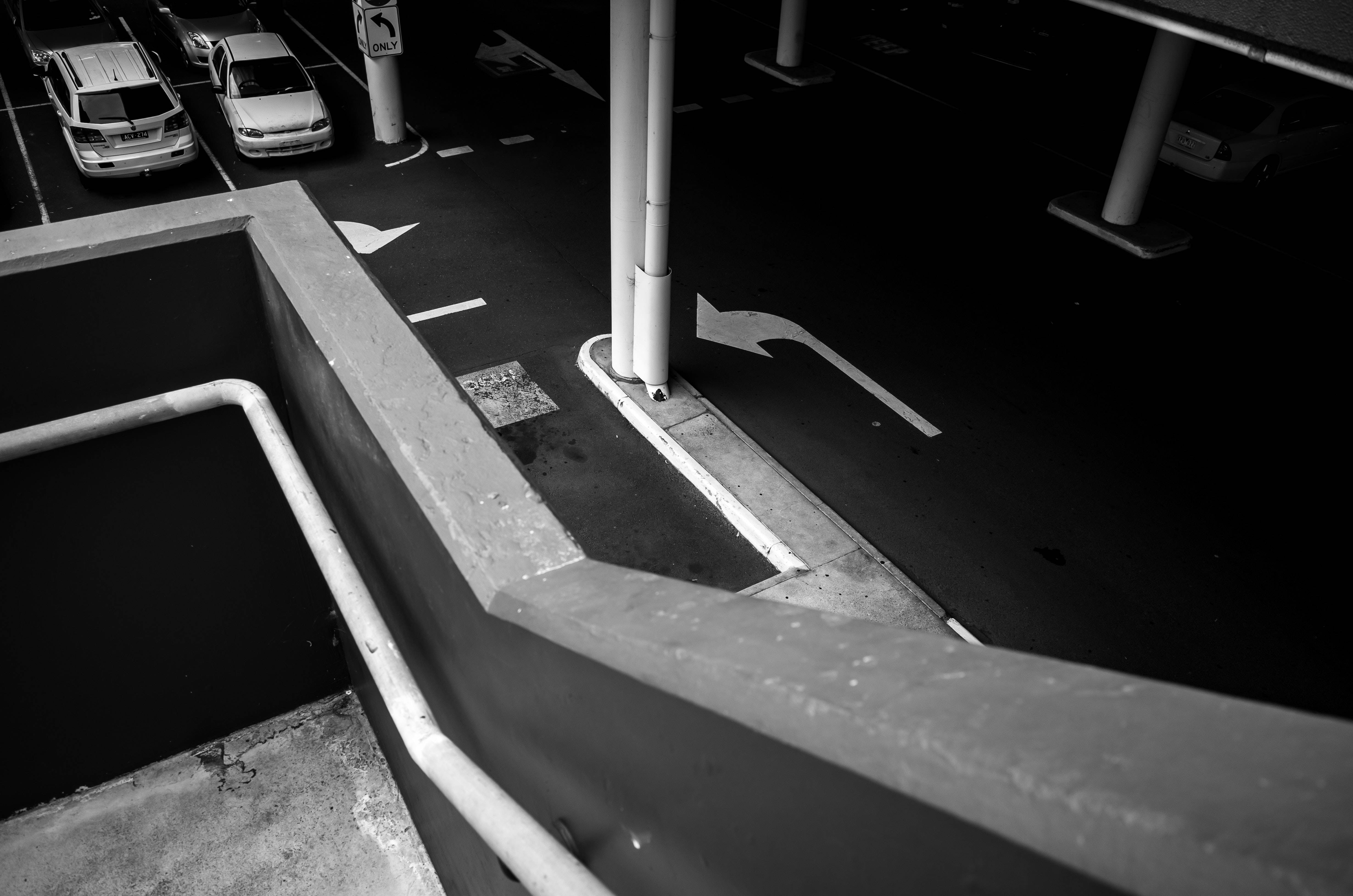 黑白 桌布 壁紙 — 高角度黑白拍攝混凝土停車場，內有車輛及方向箭頭，在人造光線下。