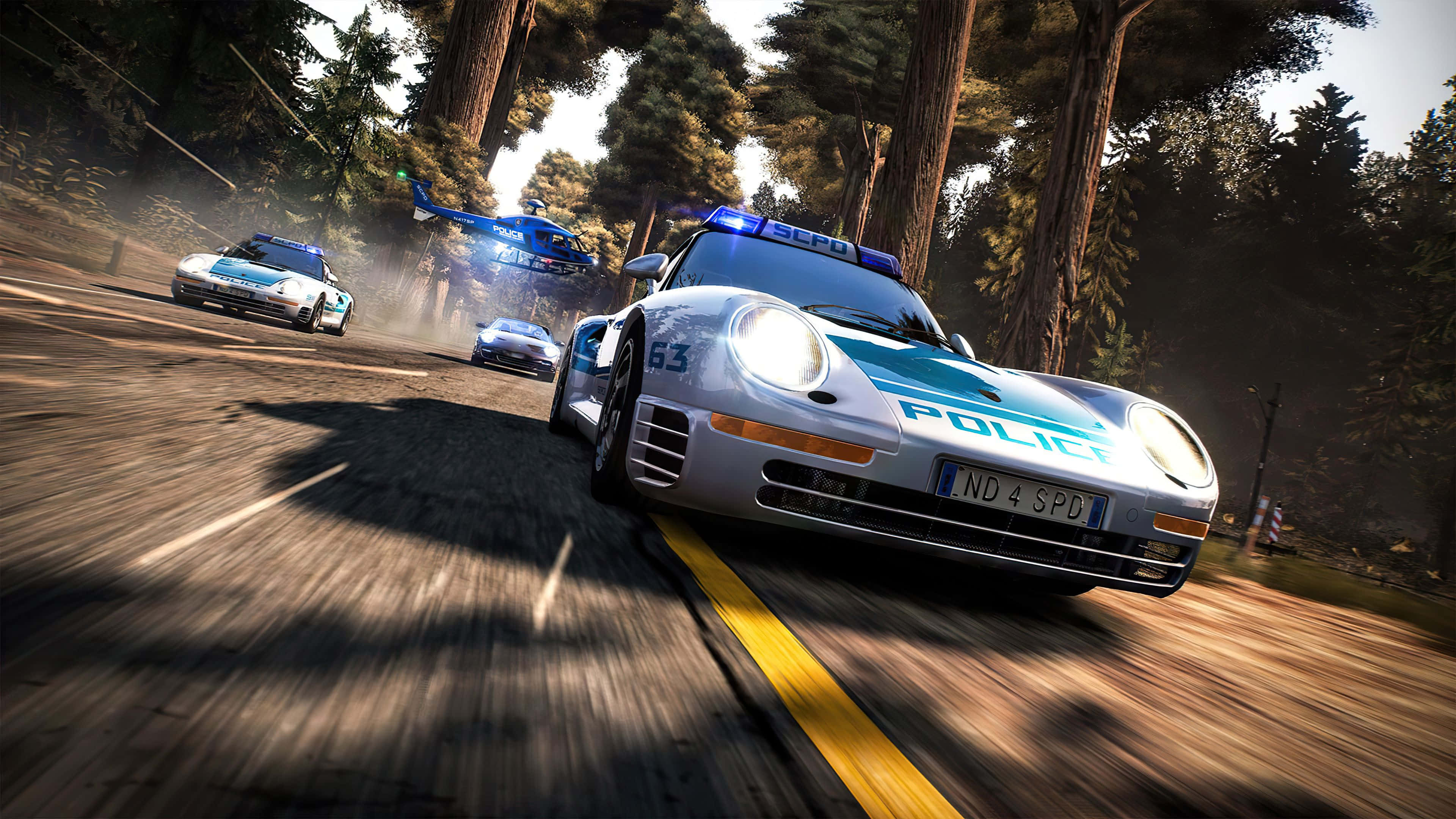Best Need For Speed 桌布 壁紙 — 高速警匪追逐在森林道路上展開，一架藍色直升機在上空盤旋，賽車後方塵土飛揚。