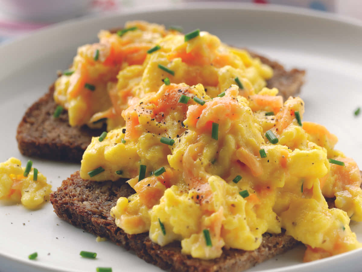 Scrambled Egg 桌布 壁紙 — 鬆軟炒蛋搭配鮭魚和細香蔥，高高堆在兩片黑麥吐司上，放在白色盤子中。