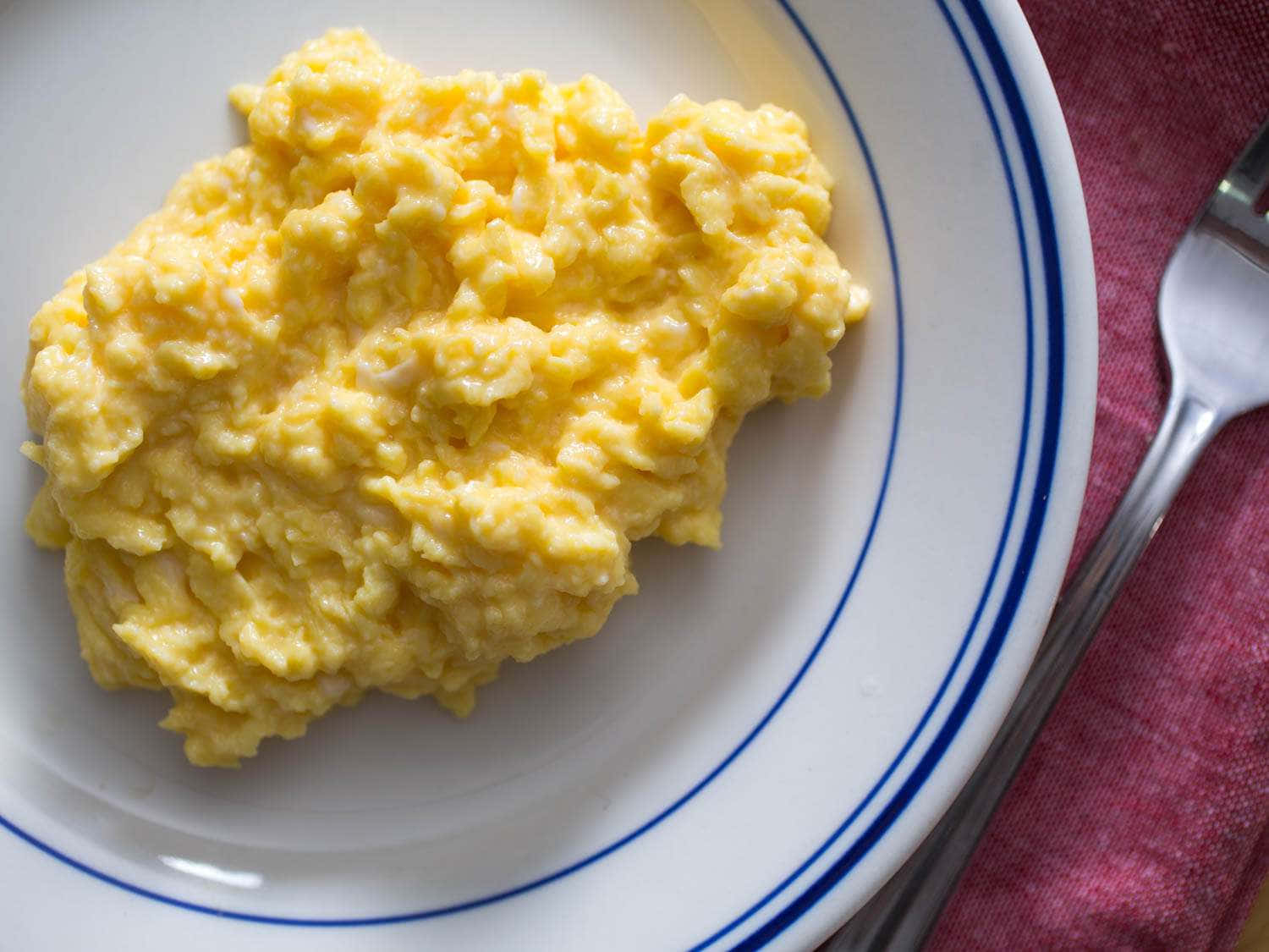 Scrambled Egg 桌布 壁紙 — 鬆軟金黃色炒蛋放在白色藍邊盤子上，旁邊有叉子，置於紅色布上。