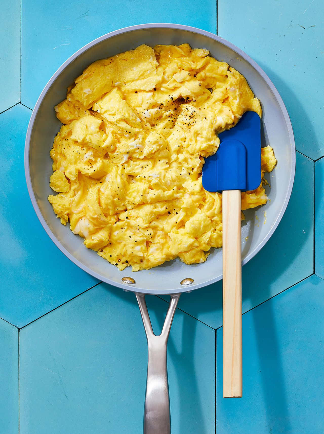 Scrambled Egg 桌布 壁紙 — 鬆軟金黃色的炒蛋，以黑胡椒調味，放在銀色平底鍋中，背景是鮮豔的藍色六角形瓷磚。