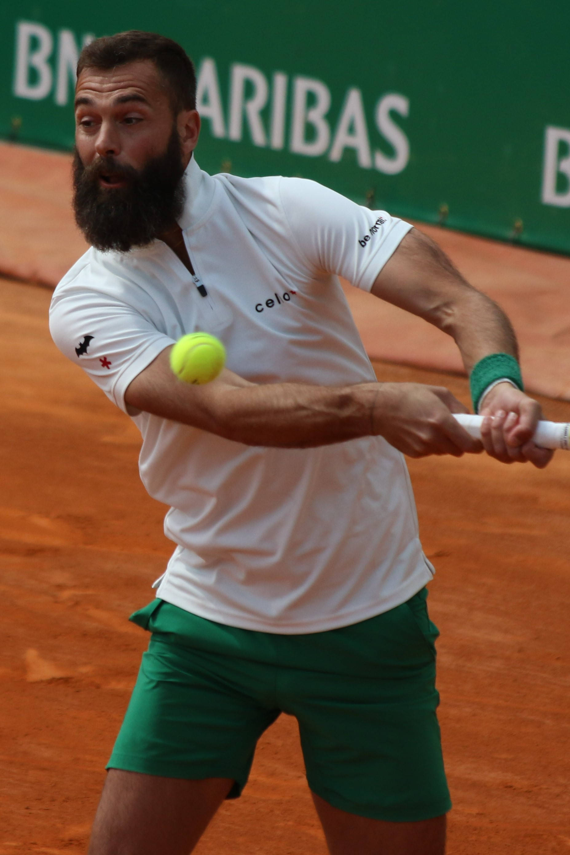 Tennis 桌布 壁紙 — 鬍鬚網球選手身穿白色襯衫和綠色短褲，在紅土球場上揮拍擊打黃色網球。