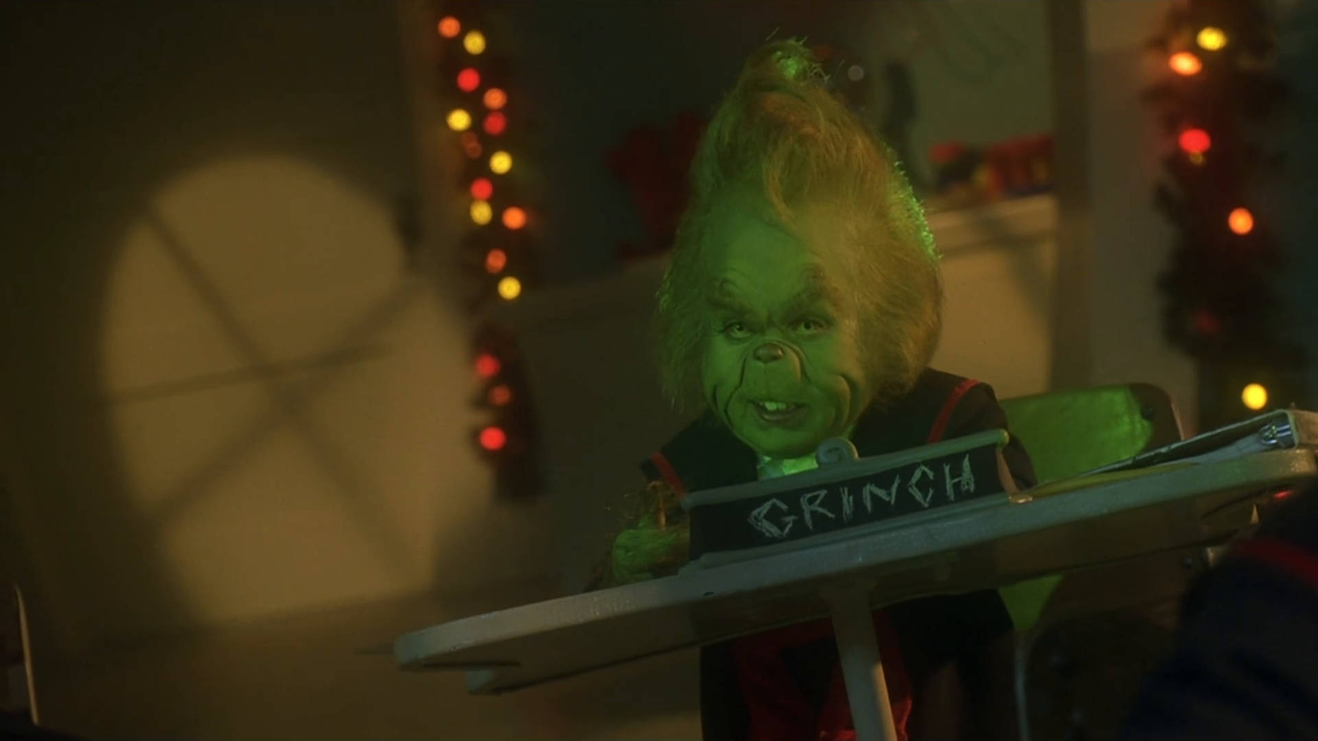 Baby Grinch 桌布 壁紙 — 鬼靈精在溫暖的節日燈光下彈奏鍵盤，背景有節日花環。