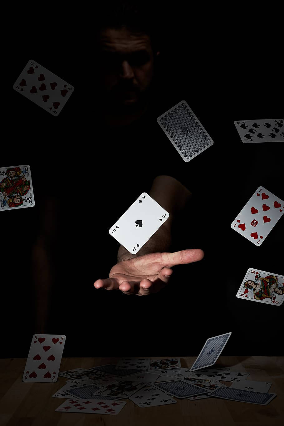 Spades 桌布 壁紙 — 魔術師的手在深色背景中懸浮於墜落的撲克牌之上，木桌上散落著紙牌。