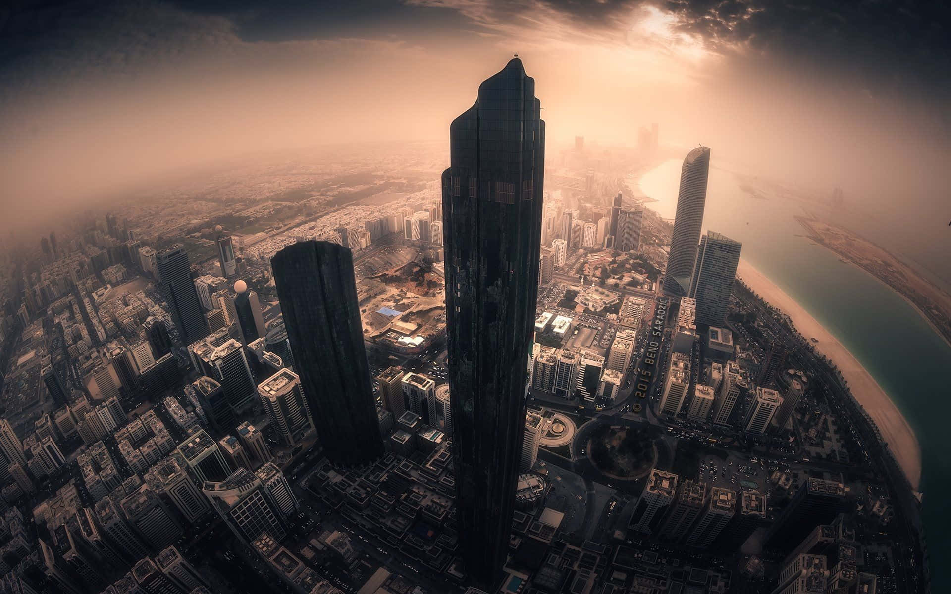Uae 桌布 壁紙 — 魚眼視角下的未來城市景觀，夕陽西下，高聳的摩天大樓和彎曲的海岸線沐浴在金色光芒中。