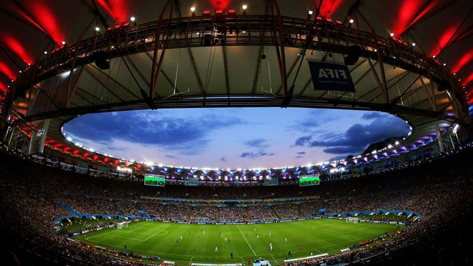 Soccer Stadium 桌布 壁紙 — 魚眼視角下的黃昏時分擠滿人的足球場，充滿活力的紅色燈光和球場上方的藍天。