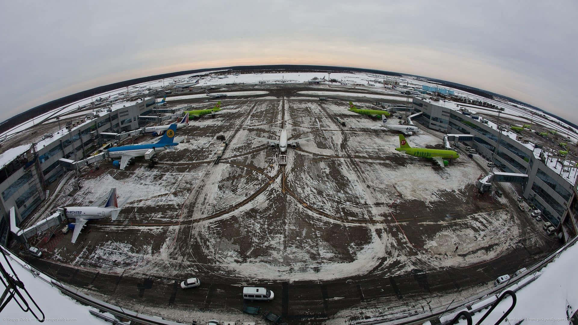 Fisheye 桌布 壁紙 — 魚眼鏡頭下的雪地機場停機坪，黃昏時分，停泊的飛機和航廈建築在灰色天空下。