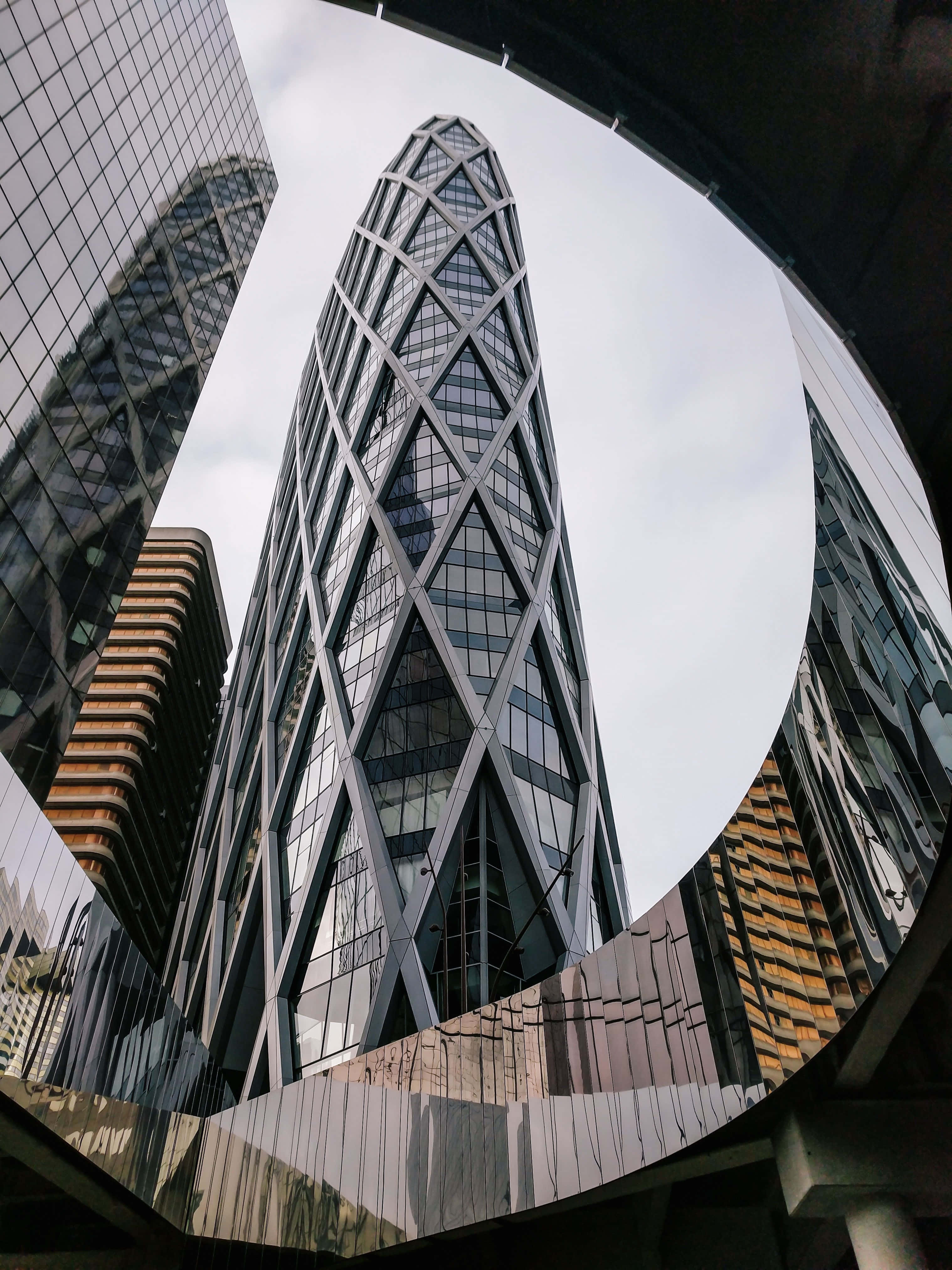 Building 桌布 壁紙 — 魚眼鏡頭捕捉到一座高聳的玻璃摩天大樓，其鑽石圖案外牆在陰天天空下反射周圍建築物。