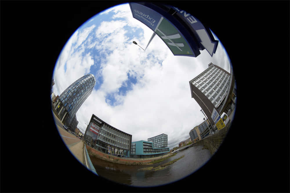 Fisheye 桌布 壁紙 — 魚眼鏡頭捕捉到扭曲的城市天際線，現代建築和陰天天空倒映在下方水中。