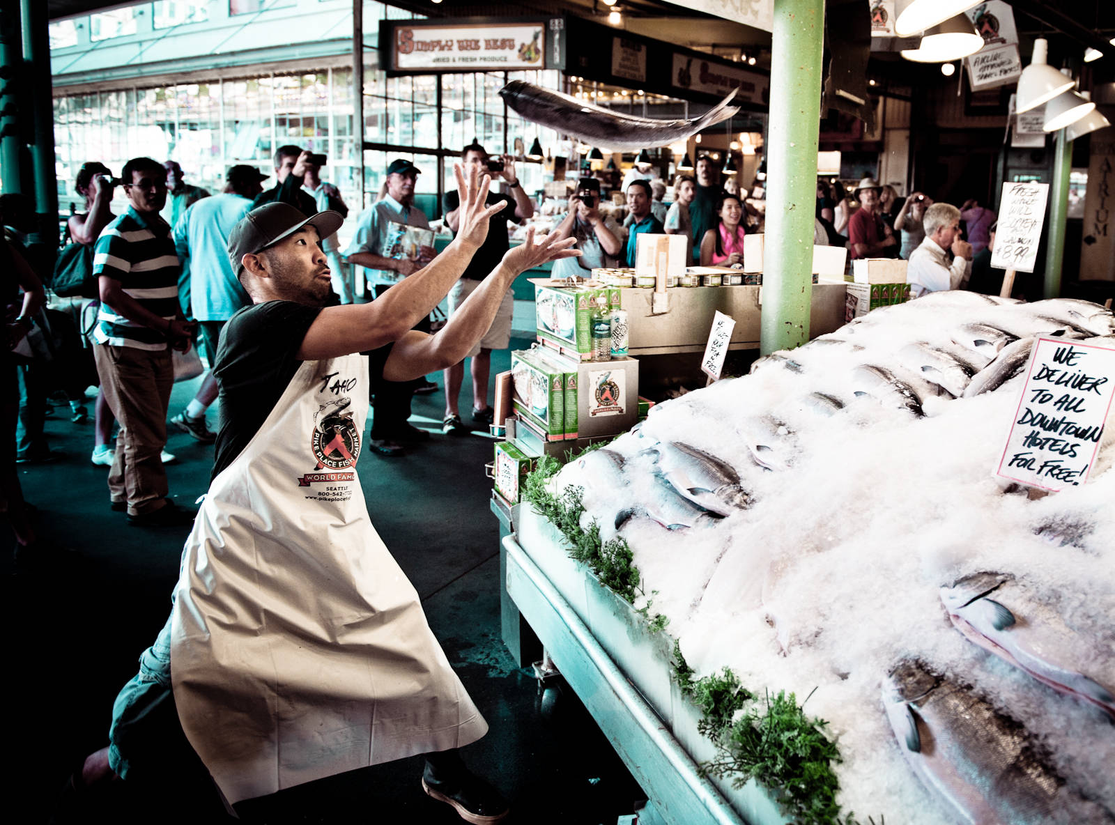 Pike Place Market 桌布 壁紙 — 魚販在熱鬧的室內海鮮市場戲劇性地拋擲一條魚，人群圍觀。