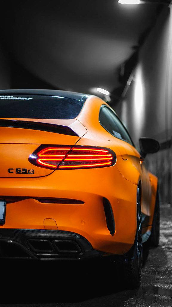 Amg 桌布 壁紙 — 鮮橙色 Mercedes-AMG C63 S 雙門跑車，帶有發光的紅色尾燈，停在光線昏暗的隧道中。