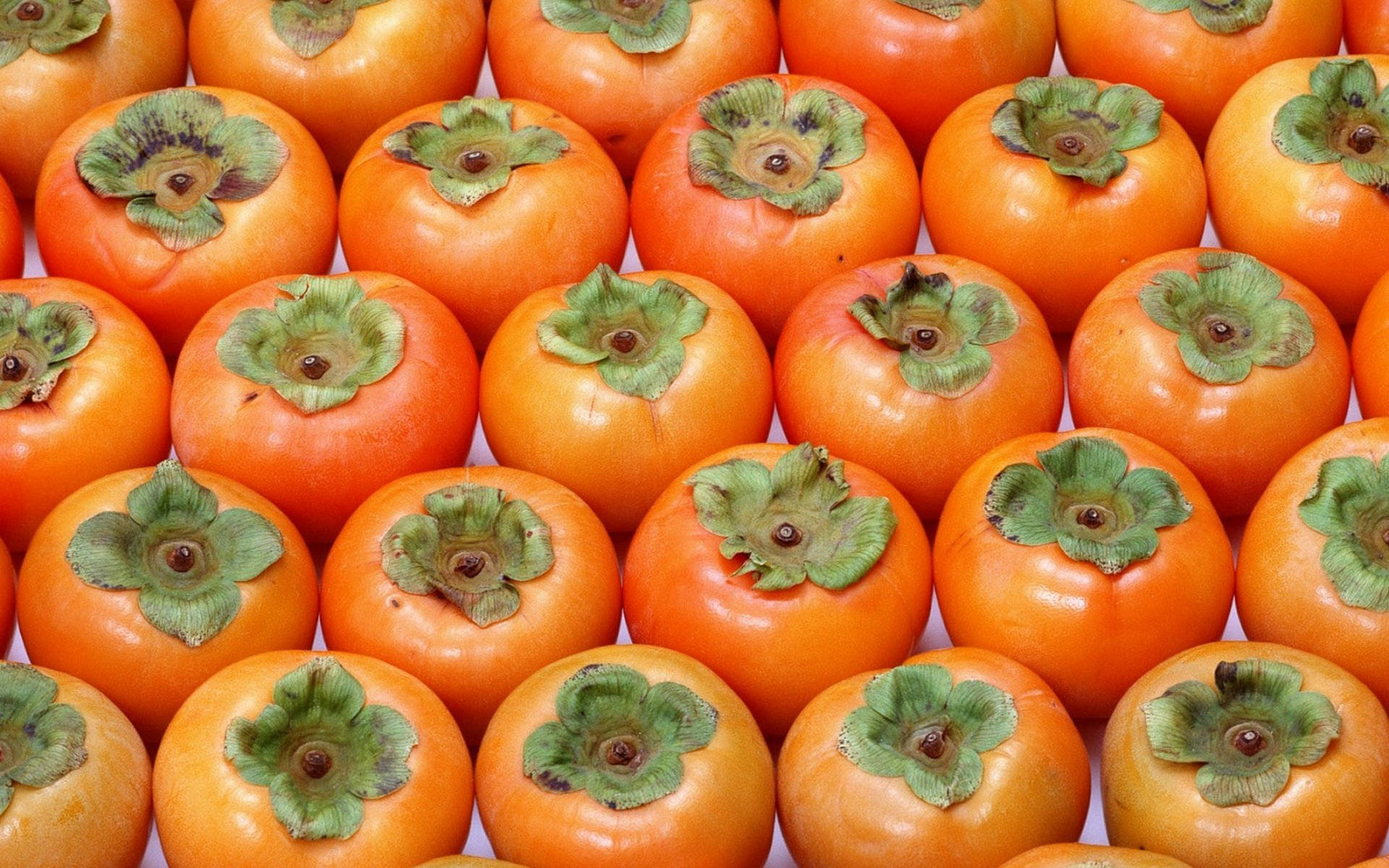 Fruit 桌布 壁紙 — 鮮橙色柿子和綠色葉帽的近距離特寫，排列成密集重複的圖案。