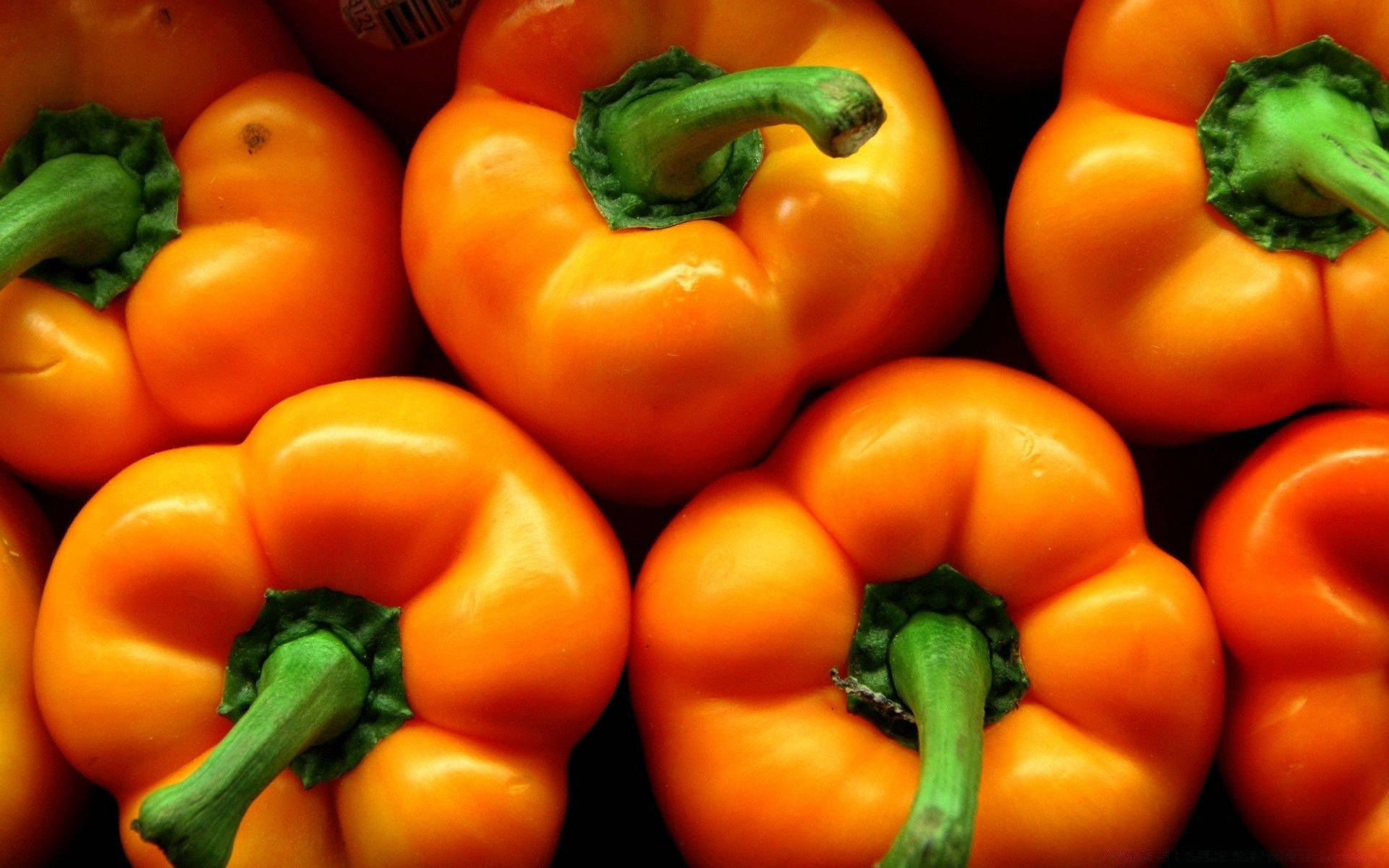Fruits 桌布 壁紙 — 鮮橙色燈籠椒，帶綠色莖，緊密堆疊在深色背景上。