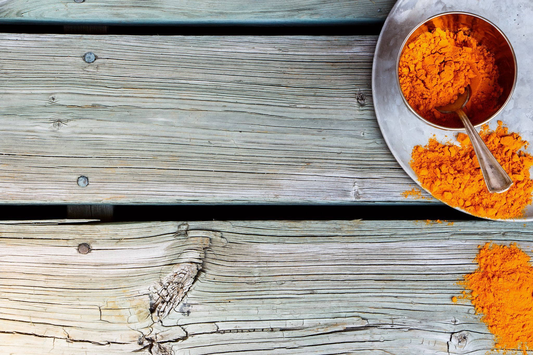 Spices 桌布 壁紙 — 鮮橙色薑黃粉從金屬碗灑落在風化的灰色木板上。