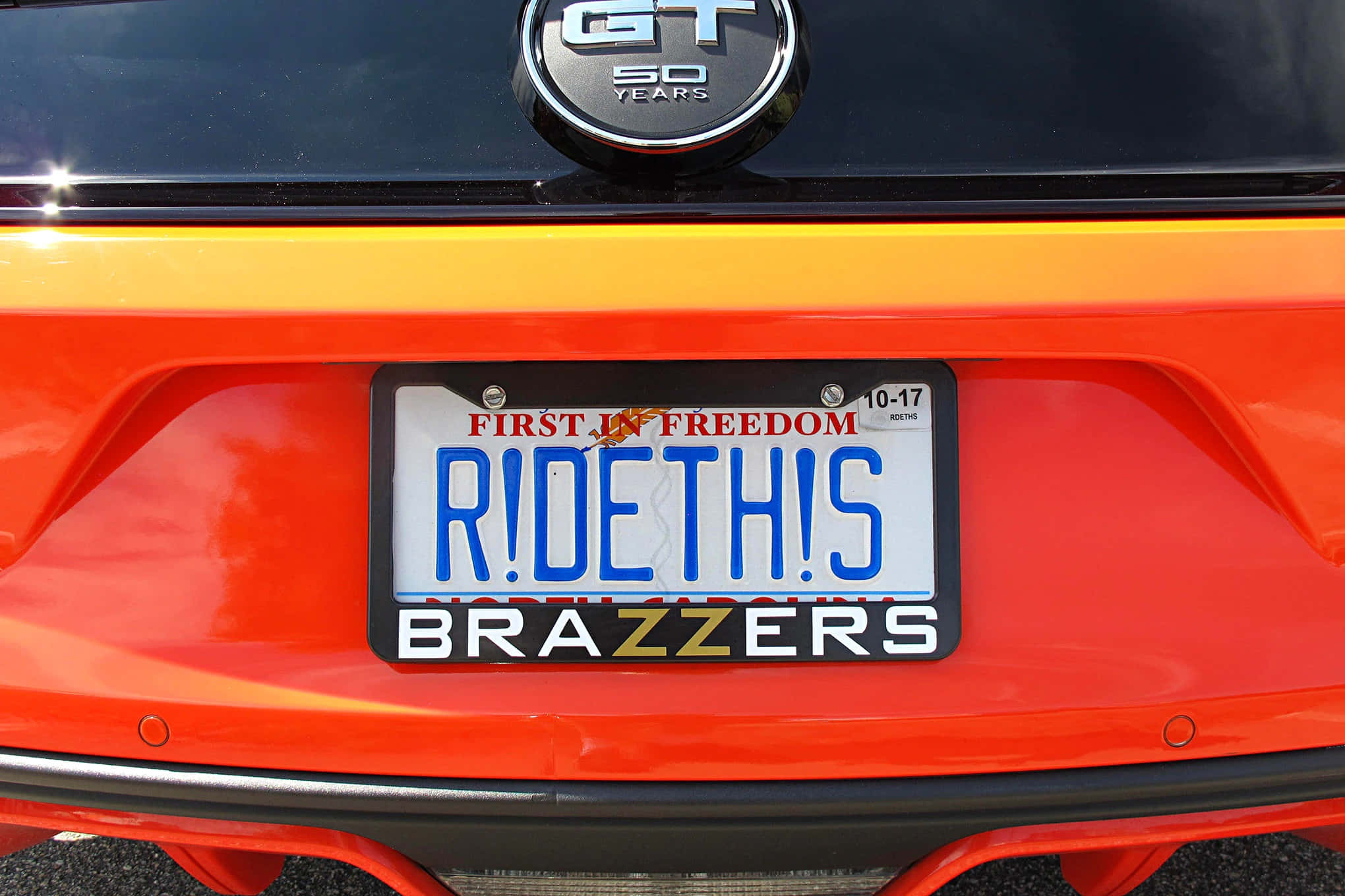 License Plate 桌布 壁紙 — 鮮橙色車尾特寫，自訂車牌上寫著 R!DETHIS，下方有 BRAZZERS。