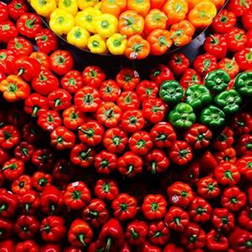 Fruit 桌布 壁紙 — 鮮紅色、黃色和綠色的甜椒高高堆疊在市場攤位上，形成色彩繽紛、質感豐富的展示。