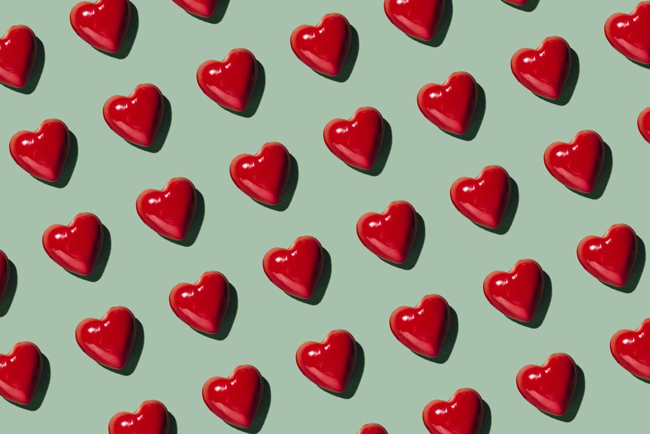 Love Heart 桌布 壁紙 — 鮮紅色亮面心形散落在柔和綠色背景上，帶有柔和陰影。